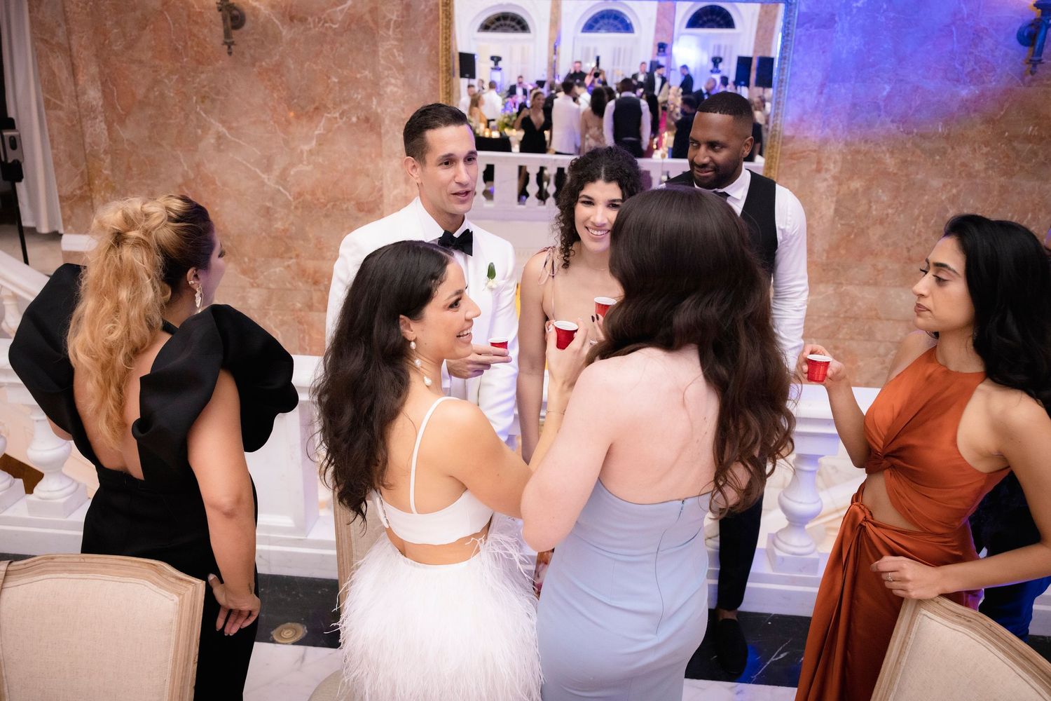 Wedding guests dance together on a crowded dance floor at an indoor reception venue.