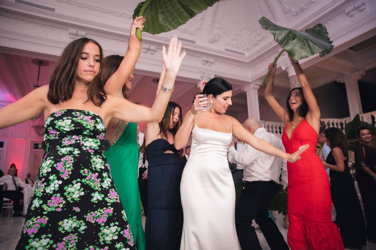 Guests enjoying themselves at a formal event with large decorative palm leaves and elegant lighting.