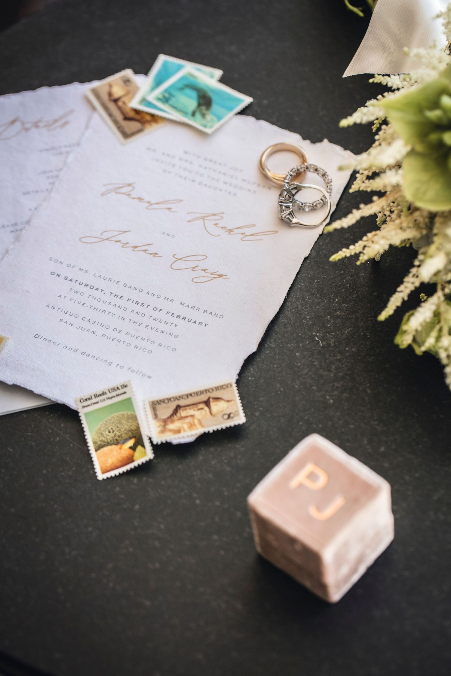 Wedding invitation details with vintage stamps and delicate floral arrangements on dark background.