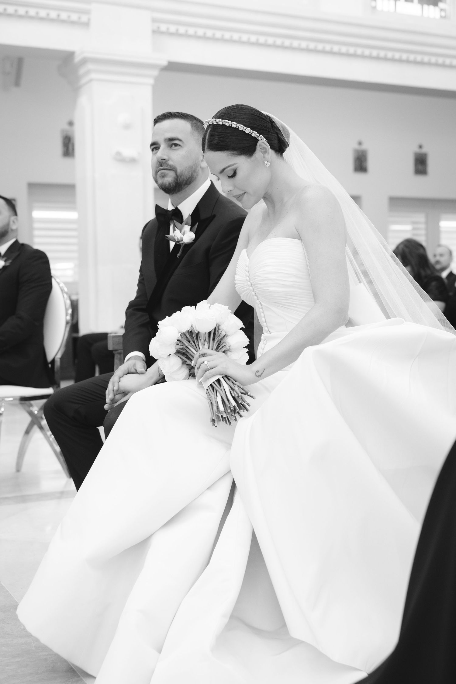 A black and white wedding photo showing a couple in classic attire seated together during their ceremony.