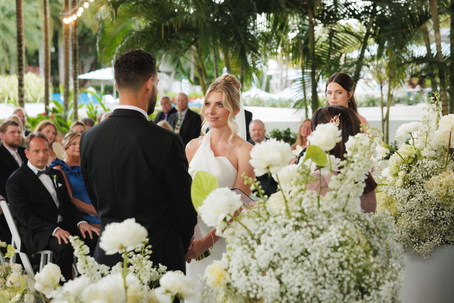 A beautiful outdoor wedding ceremony display with white floral arrangements and palm trees in the background.
