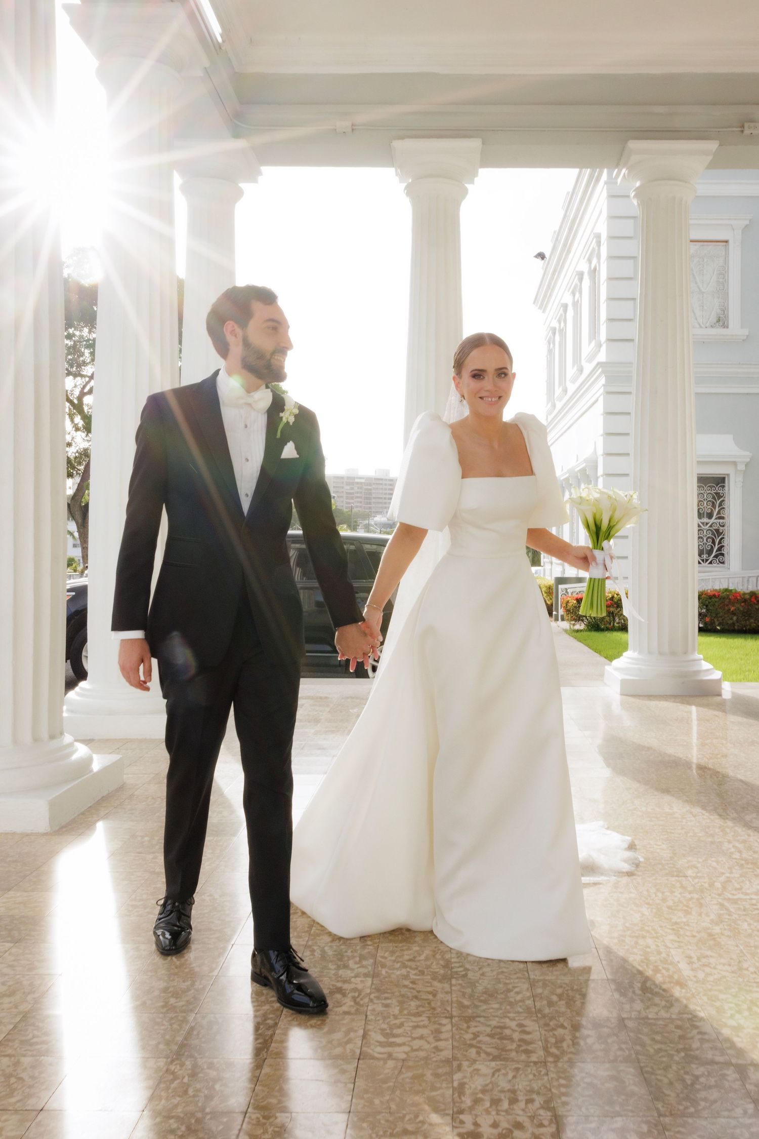 Wedding couple walking through columned porch with classic architectural details.