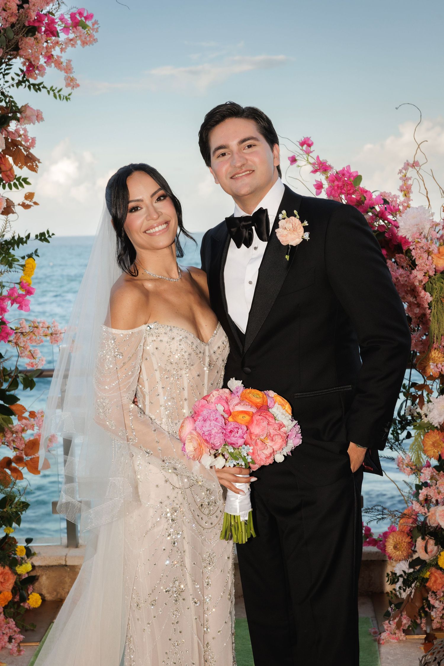 A wedding portrait series by the ocean with pink floral decor and a tropical backdrop.