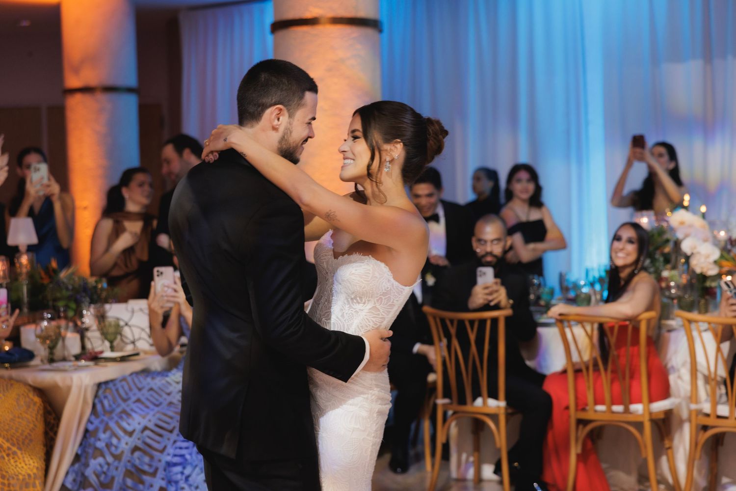 Guests dancing together at a dimly lit wedding reception with orange and blue ambient lighting.