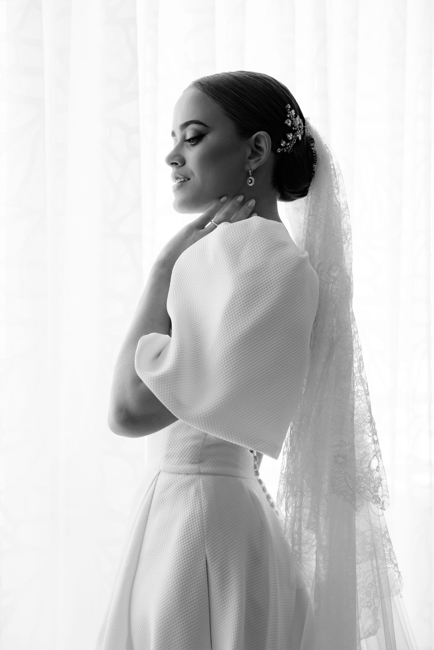 Elegant black and white bridal portrait with delicate hair accessories and dramatic lighting near a sheer curtain.