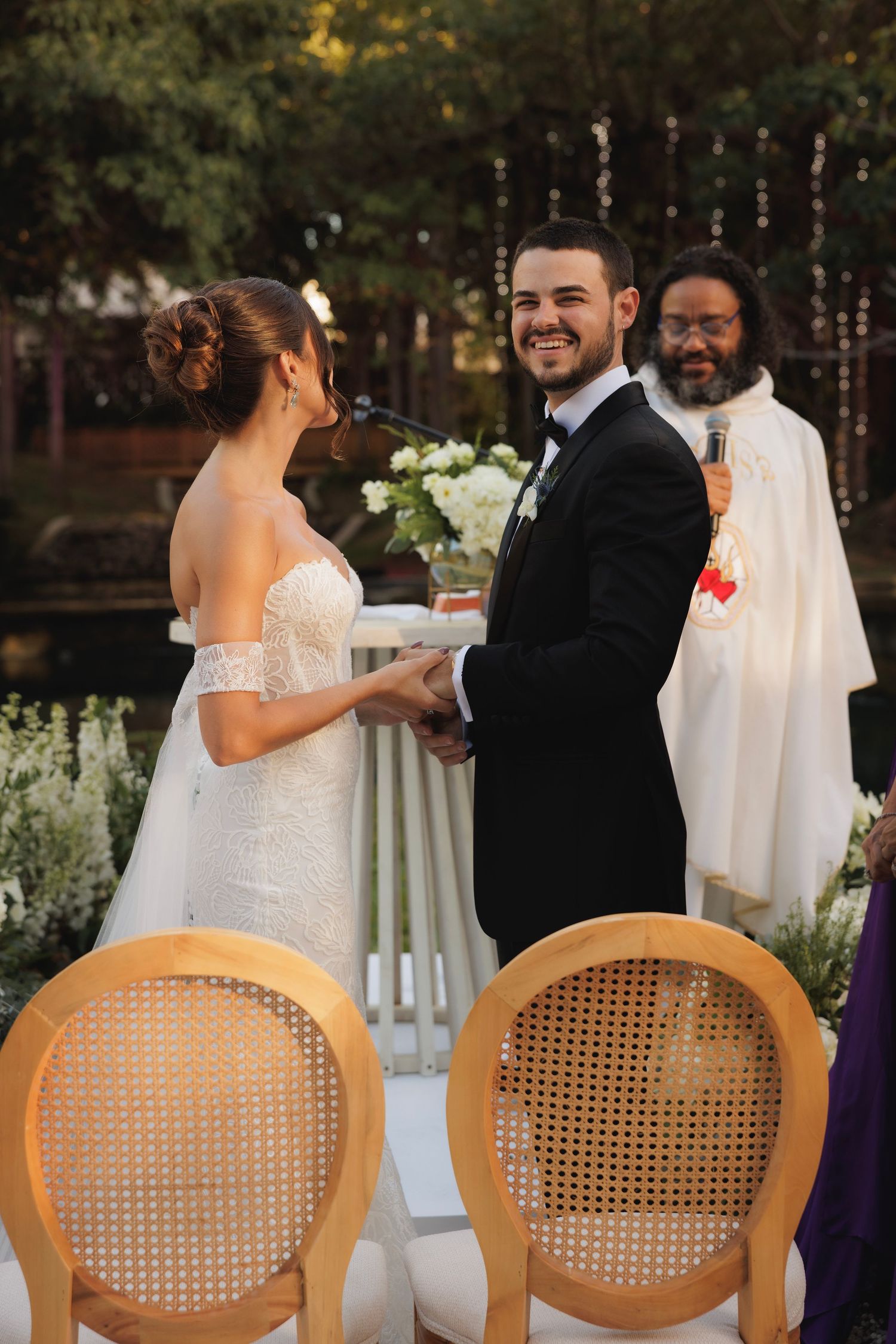 Wedding ceremony seating with natural cane chairs and floral arrangements at sunset.