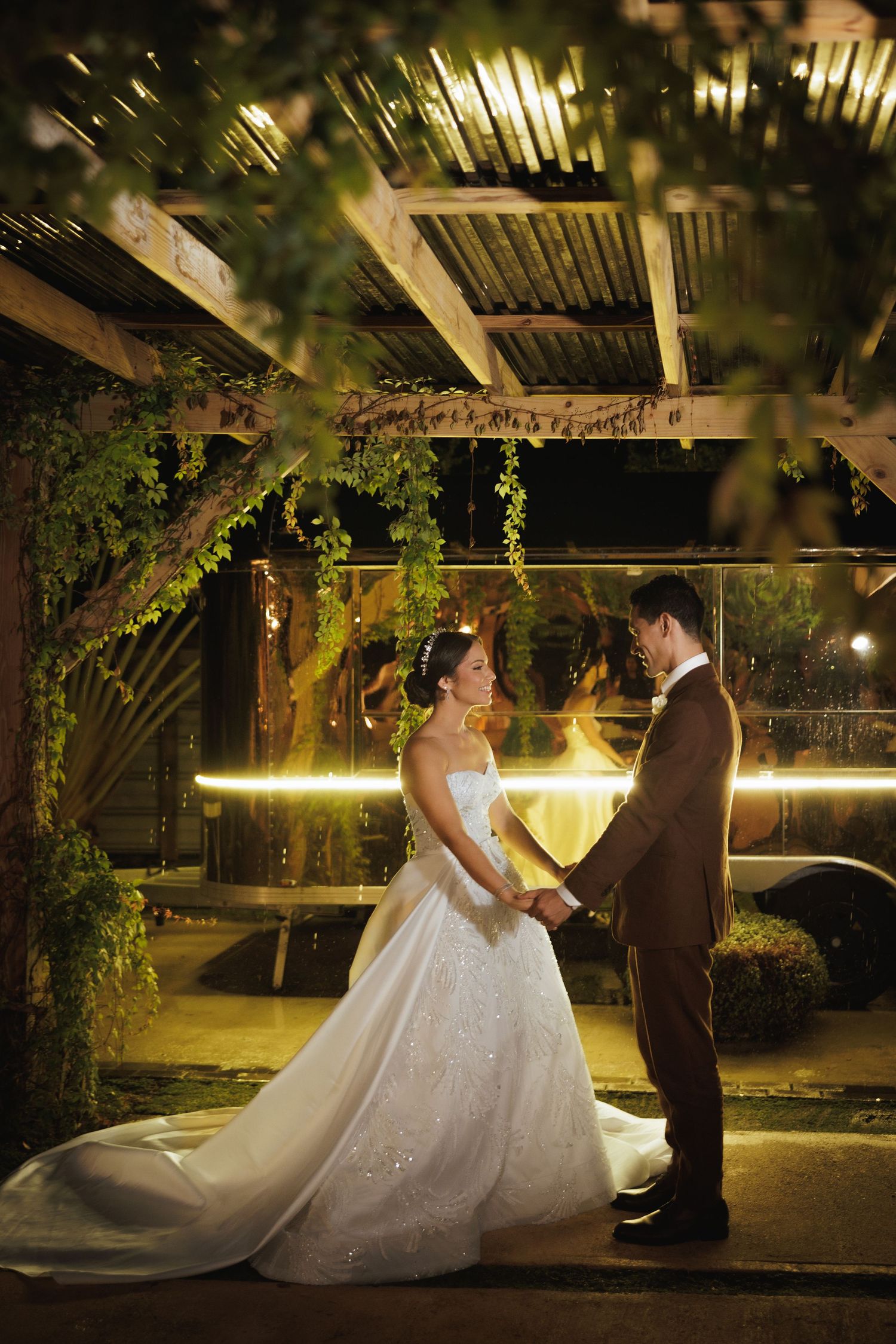 Romantic wedding couple dances under twinkling lights in an outdoor garden setting at night.
