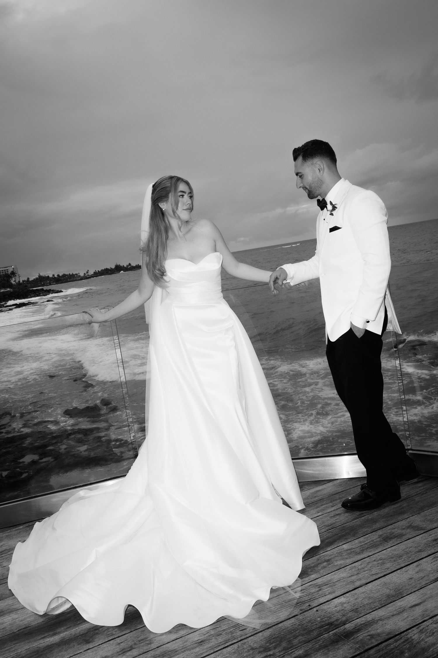 A series of black and white wedding photos showing a couple on a wooden deck by the ocean during their special day.