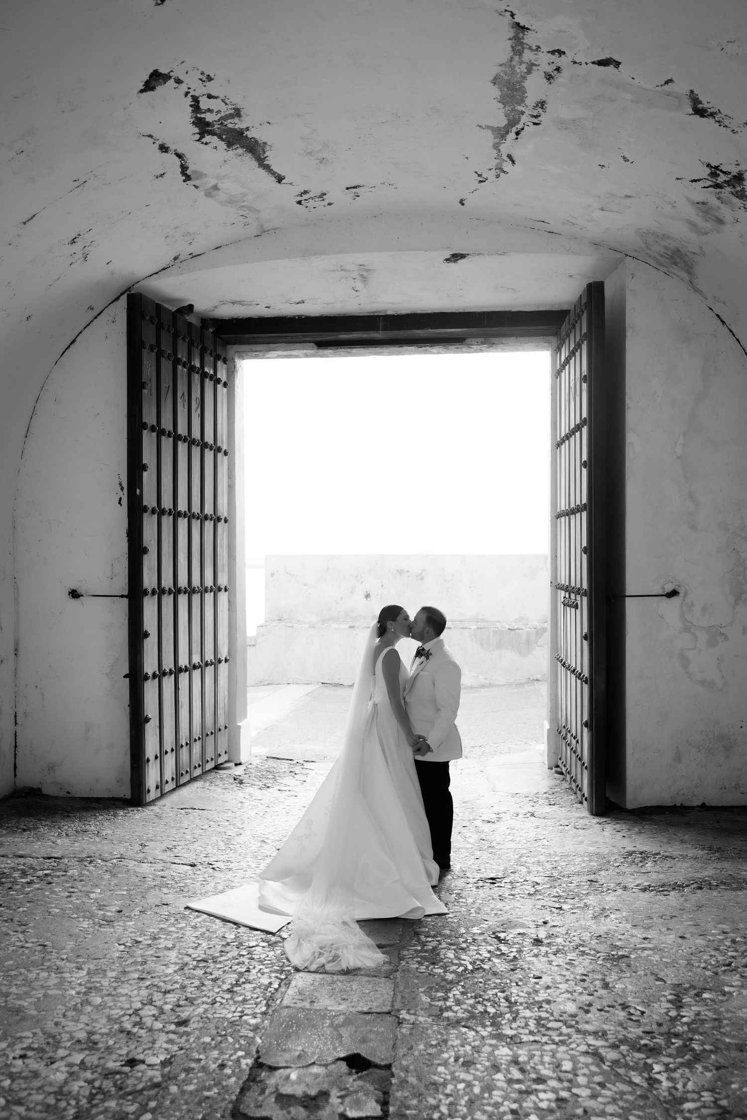 Black and white wedding photos in an arched stone passageway with dramatic lighting.