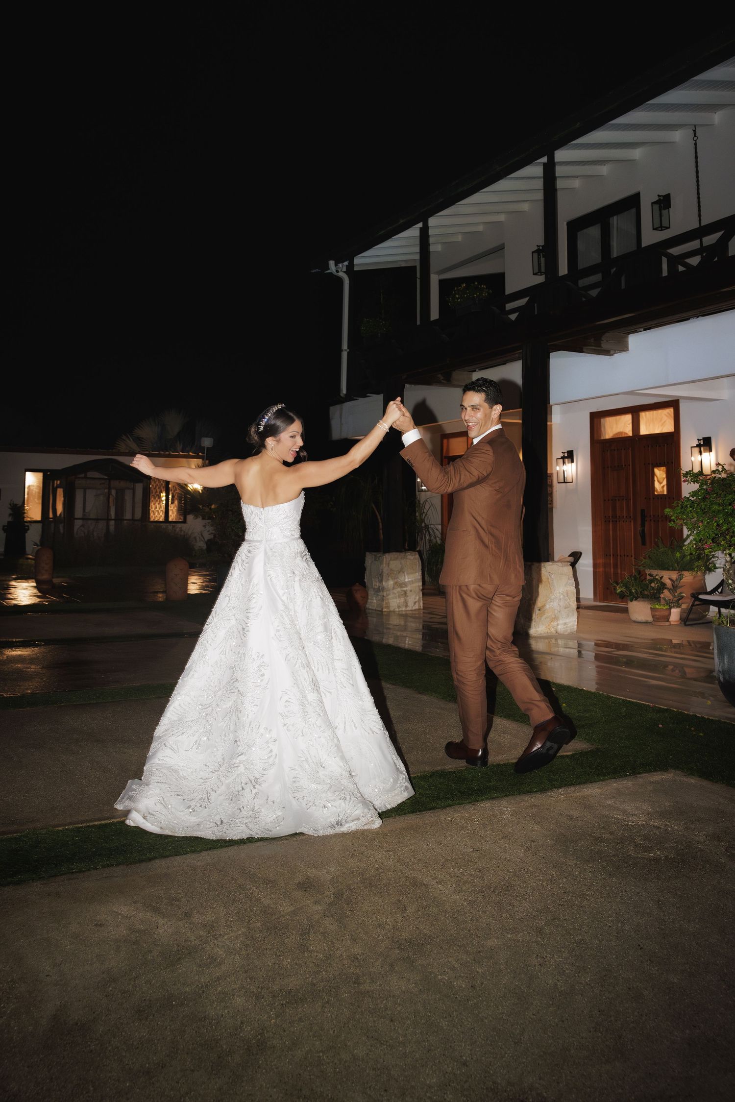 A playful wedding couple dancing and twirling outdoors at night.