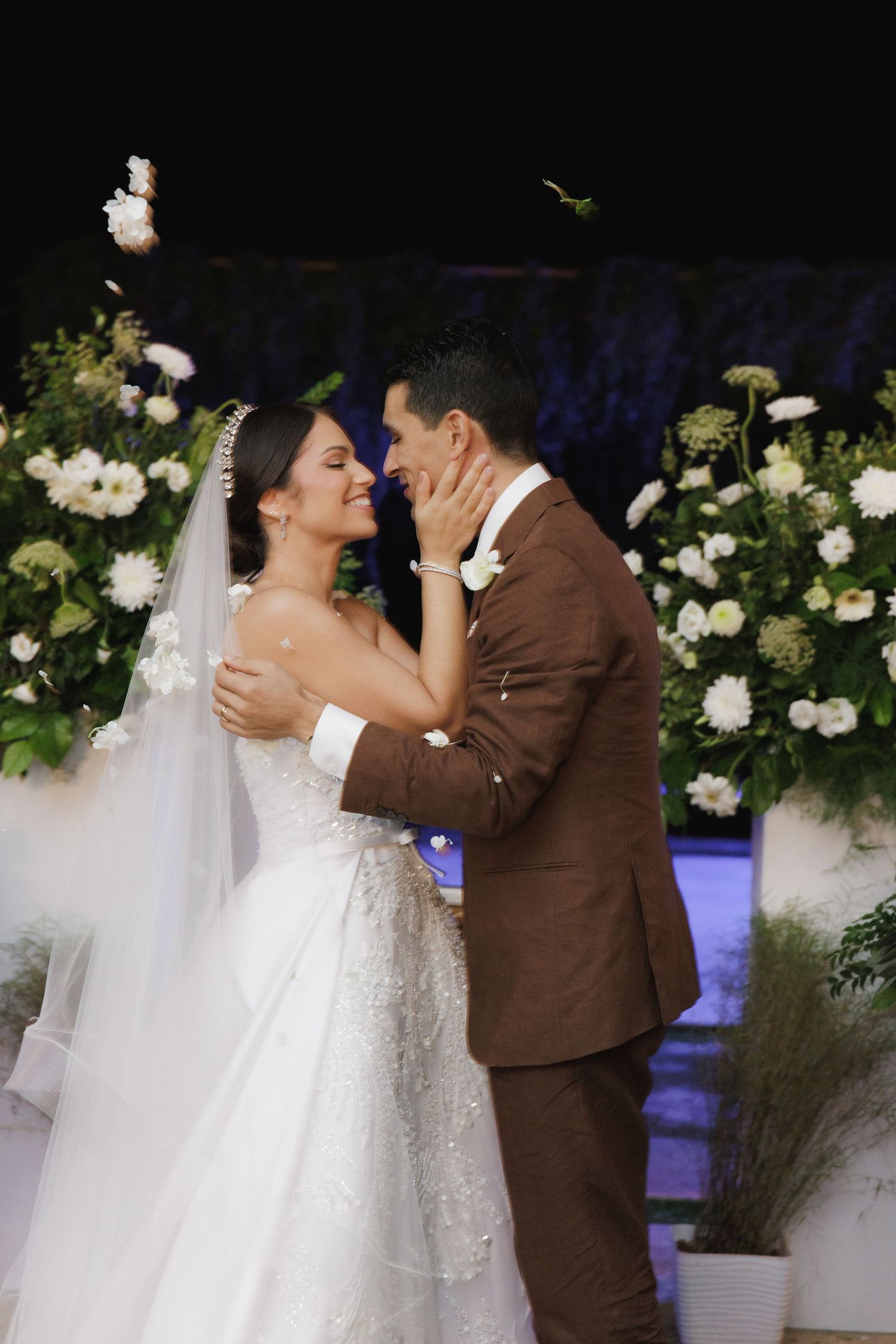 A romantic wedding moment surrounded by white floral arrangements and ambient lighting.