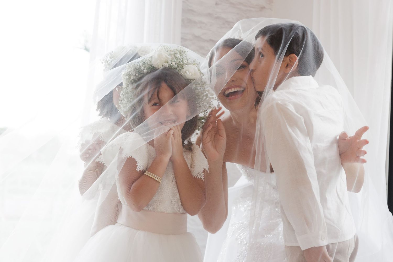 Two people share a joyful moment under flowing white veils during a wedding celebration.