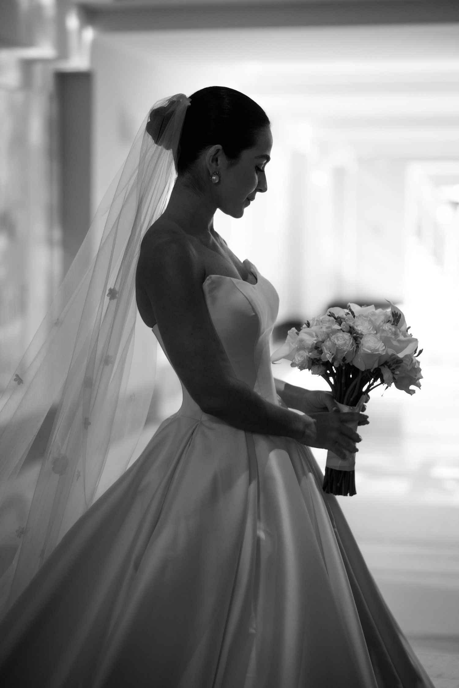 Silhouette series of a bride in a ballgown holding a bouquet near bright windows.