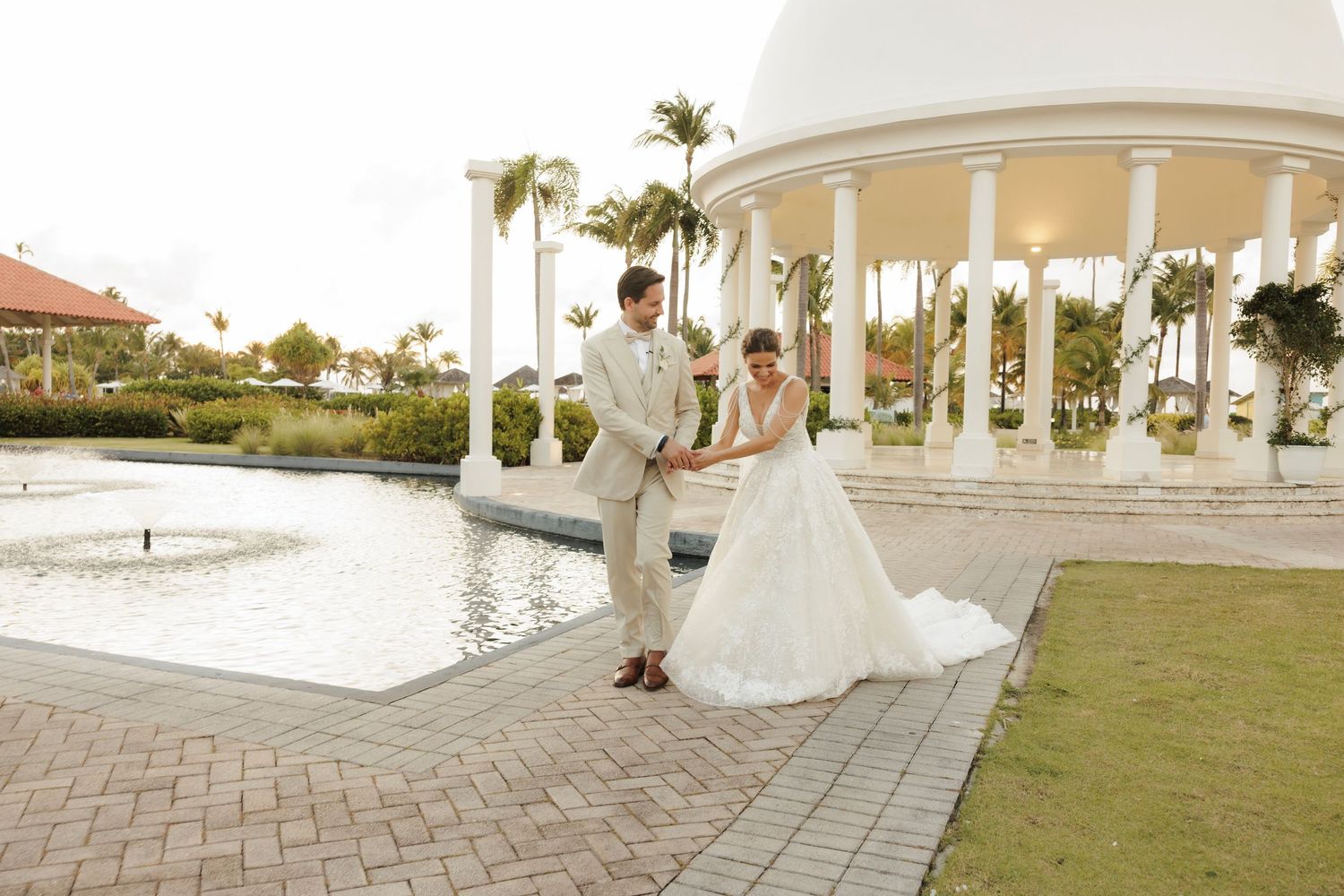 A landscaped waterfront wedding venue with white columns, arches and palm trees along a shoreline.