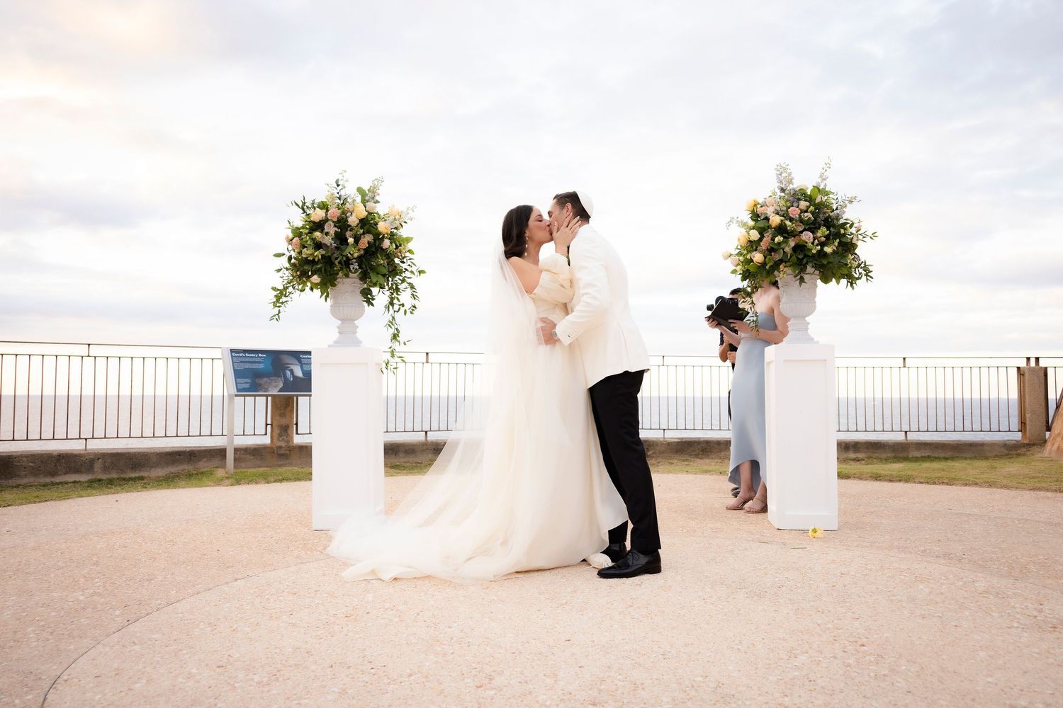 Wedding ceremony taking place on an outdoor terrace with white floral arrangements.