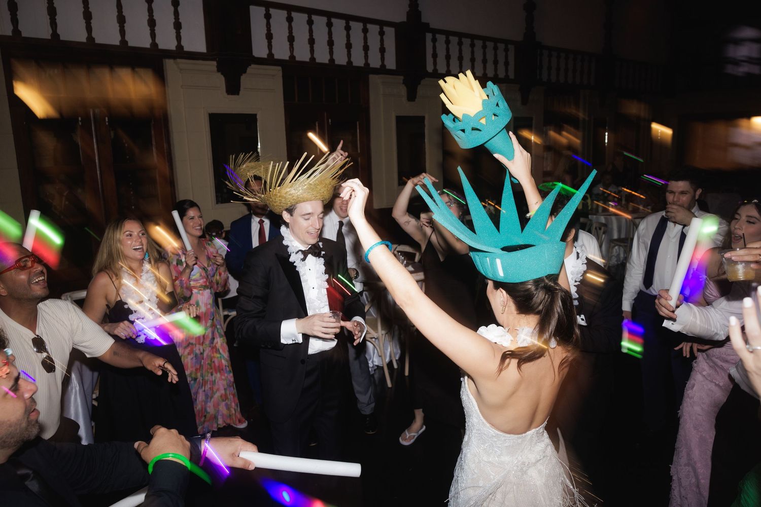 Wedding guests dance with glow sticks and light-up props on a dark dance floor during a festive reception celebration.