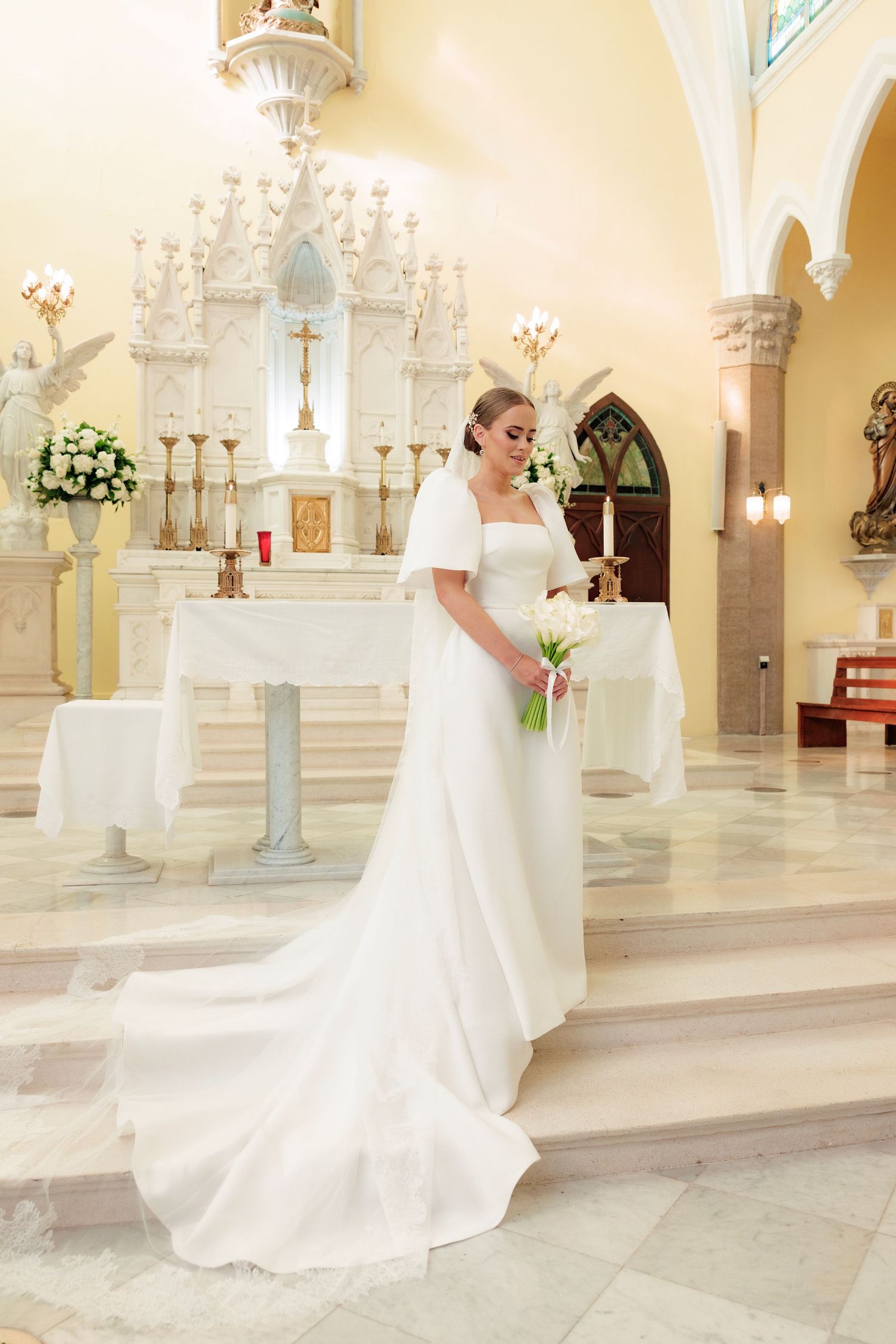 An elegant bride in a classic white gown stands at the church altar surrounded by ornate decor and floral arrangements.