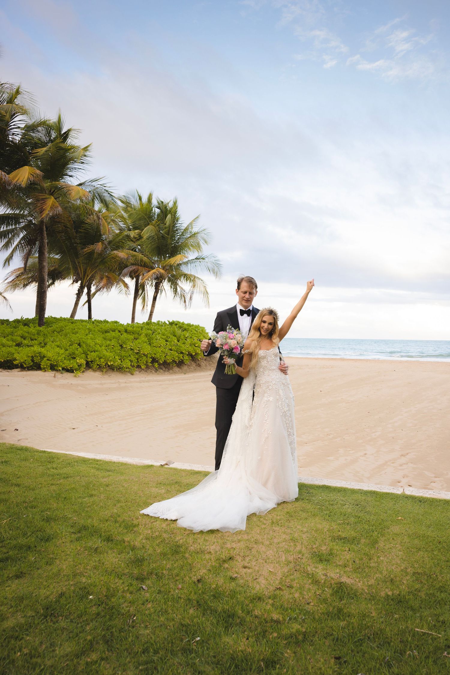 Happy newlyweds celebrate on a tropical beach with palm trees and ocean views at their destination wedding.