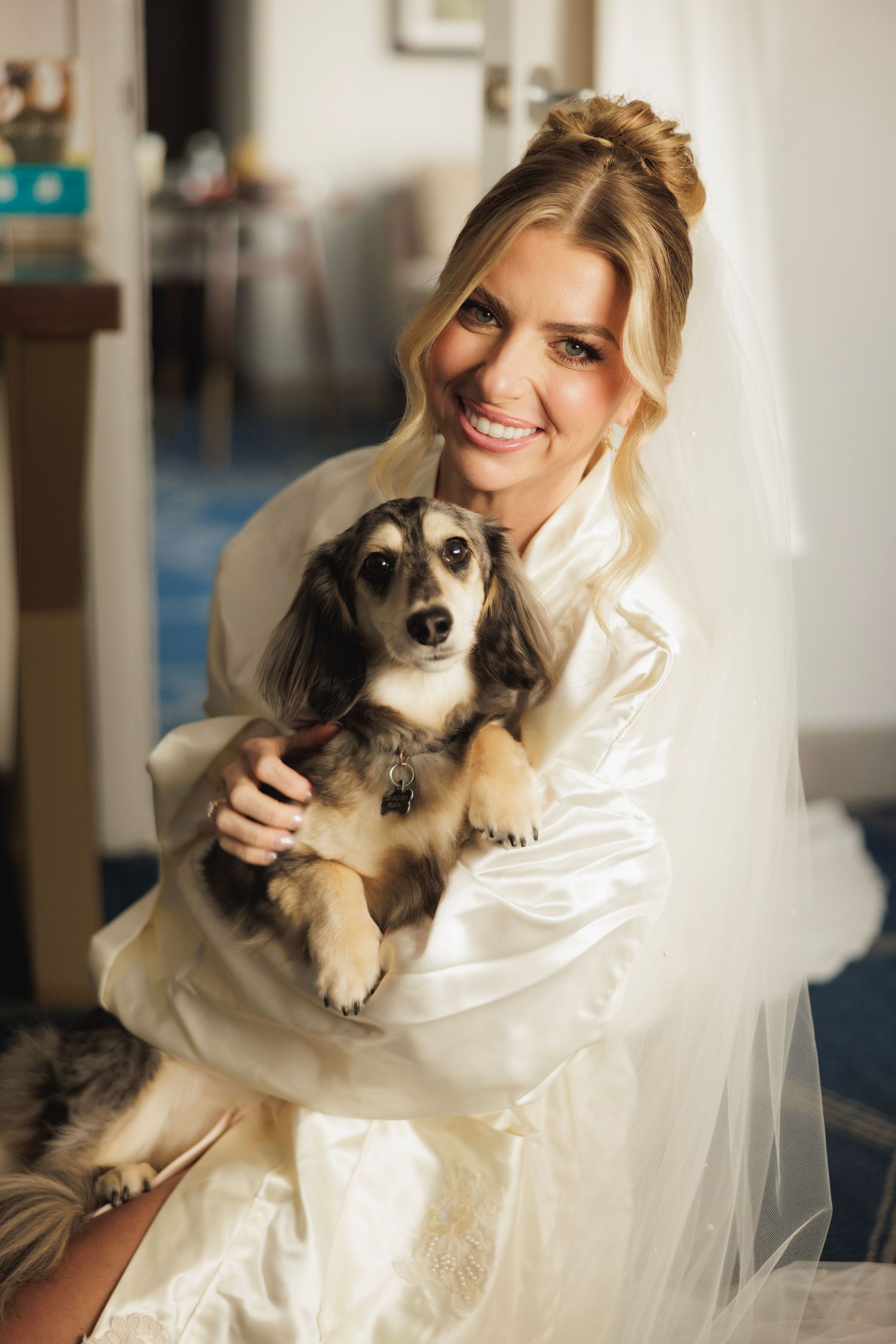 Sweet puppy being held by someone in a white wedding dress and veil during bridal preparations.