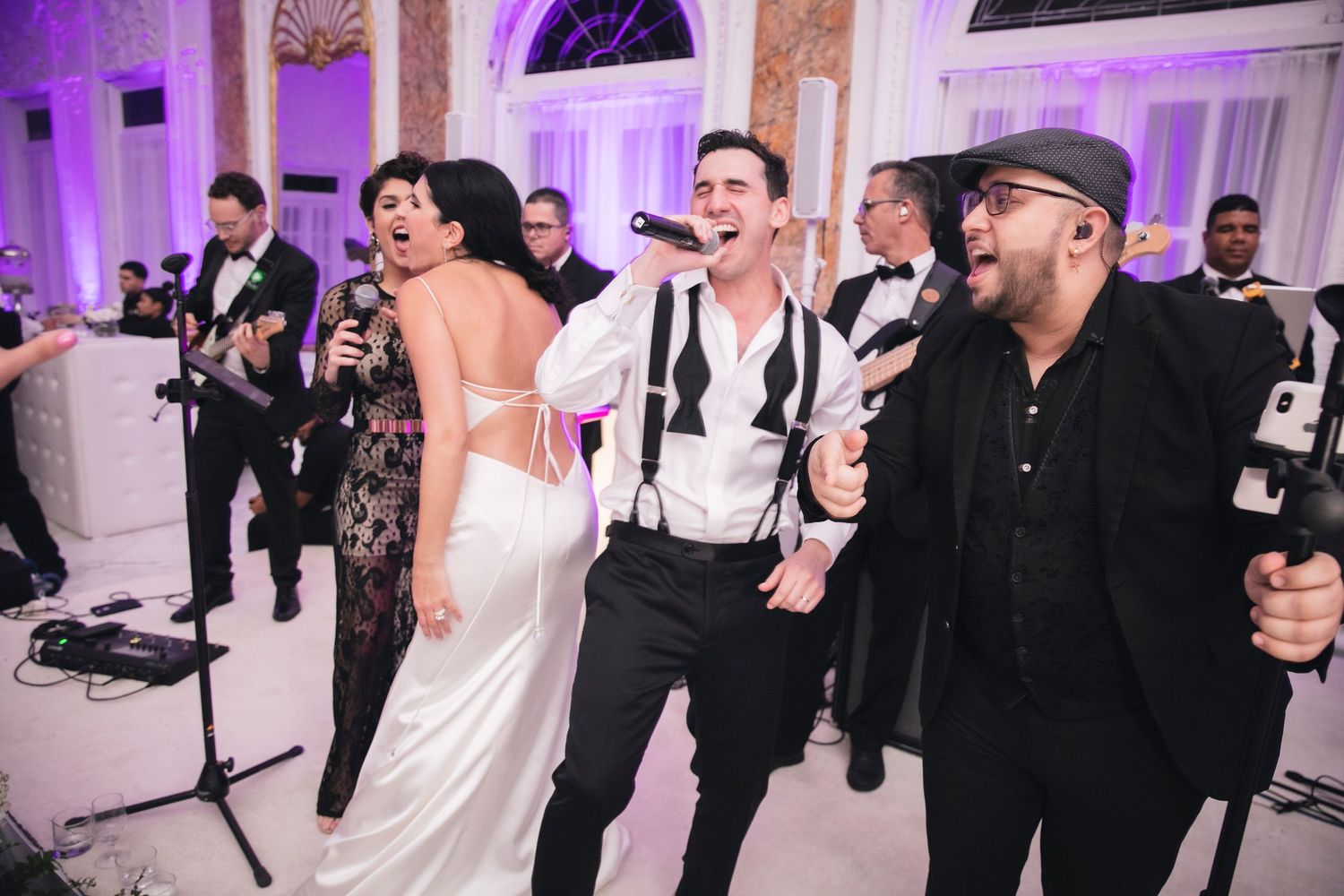 Wedding guests dance and celebrate on a purple-lit dance floor at an elegant white reception venue.