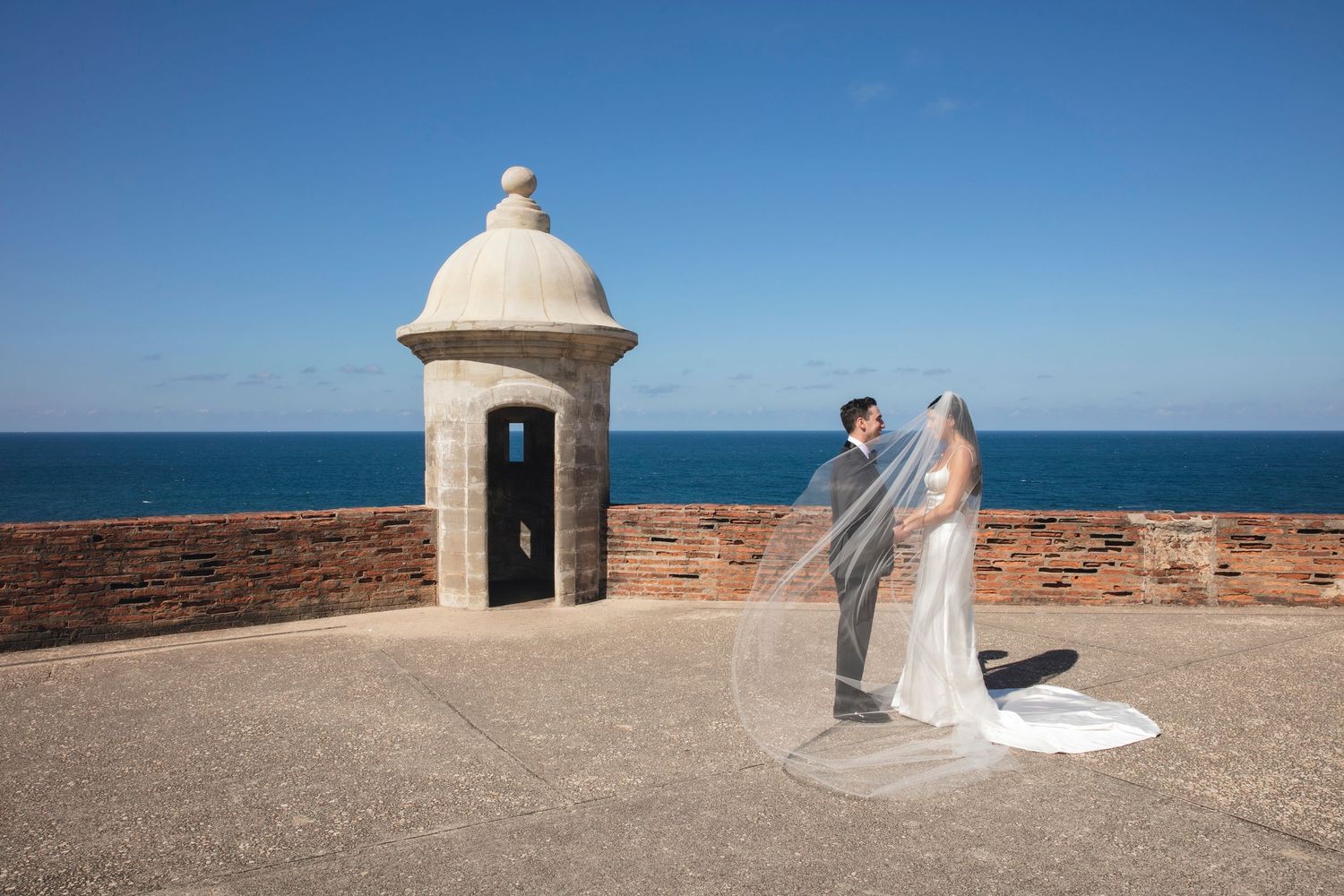 Wedding couple photographed at historical stone fortress with dramatic ocean views.