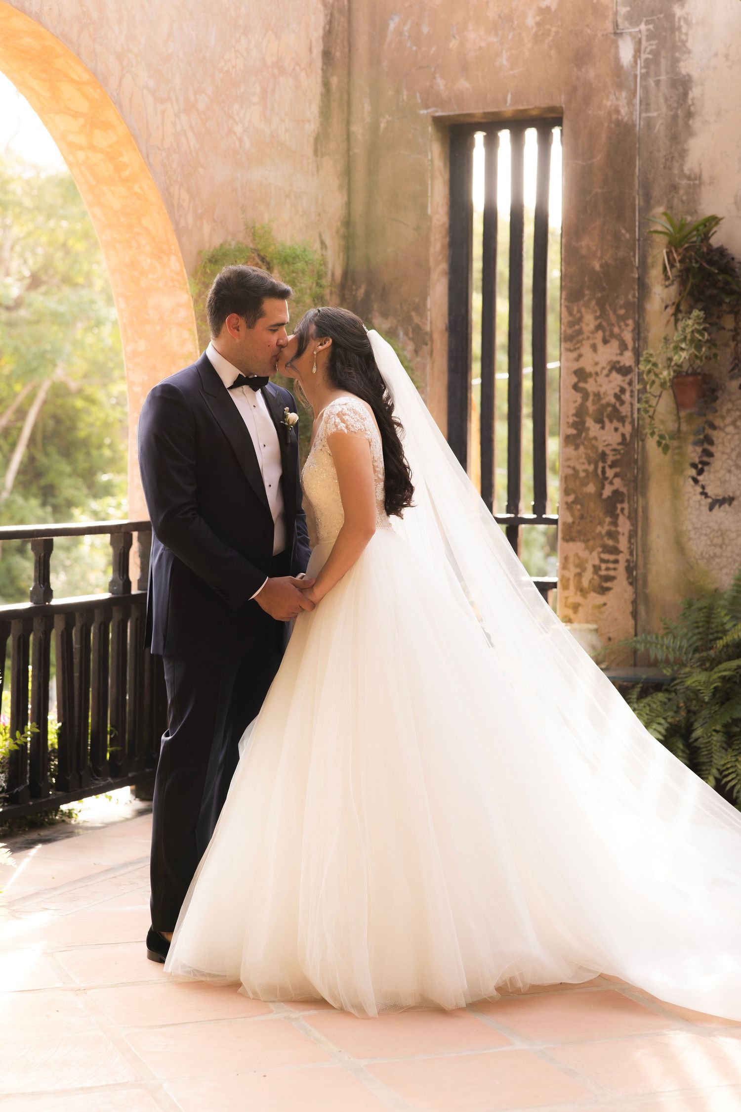 Wedding couple in formal attire sharing a romantic moment under rustic stone archways.