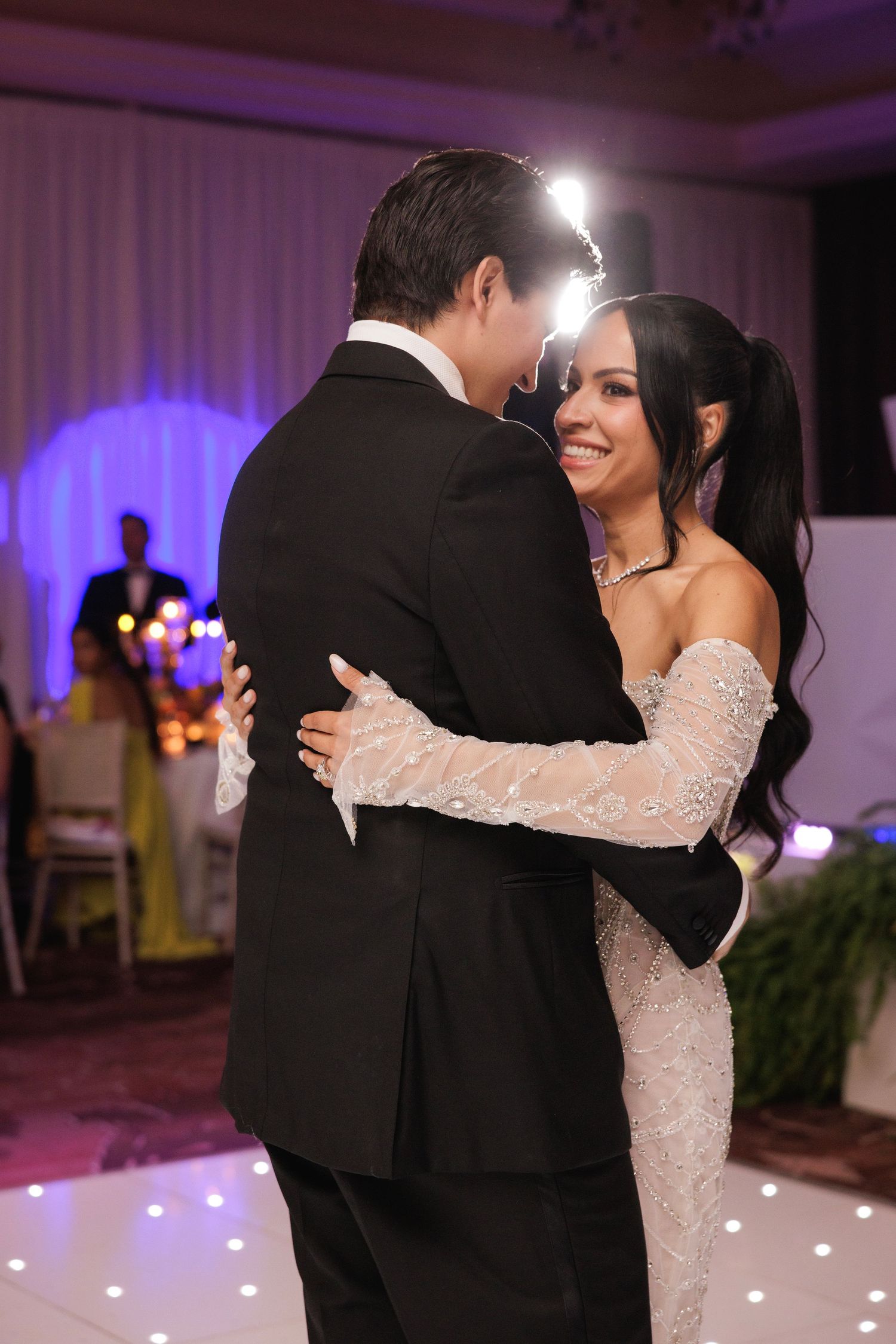 A romantic first dance at a wedding reception with purple lighting and a white dance floor.