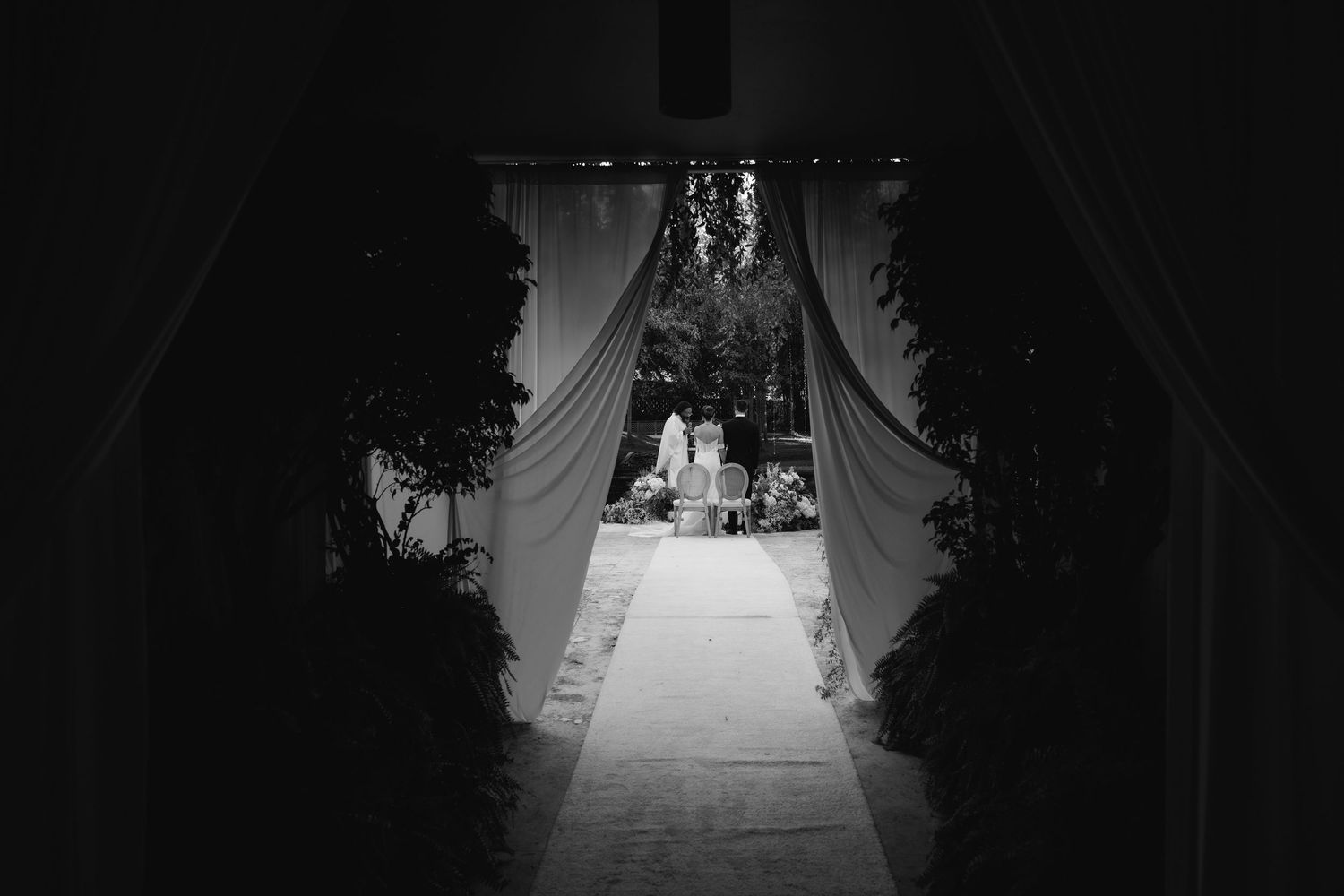 A black and white view through a draped archway leading to a bright outdoor reception area.