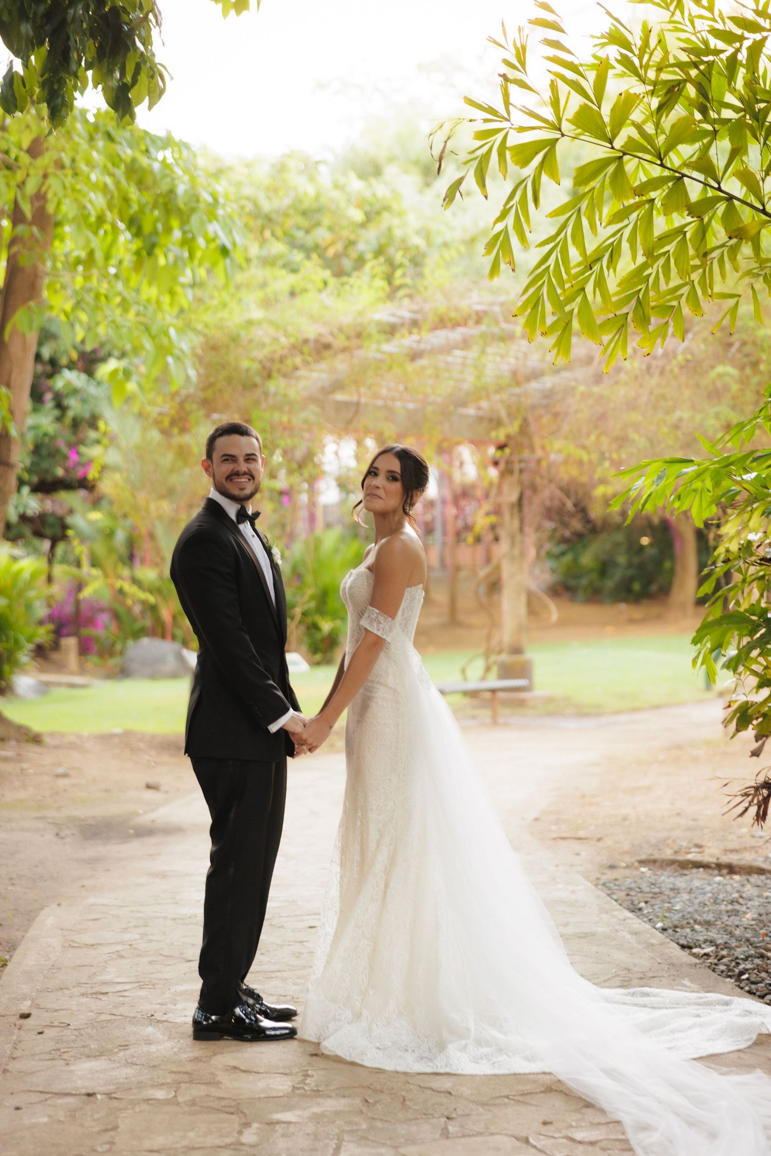 A joyful wedding couple poses for photos in a lush garden setting with natural lighting.