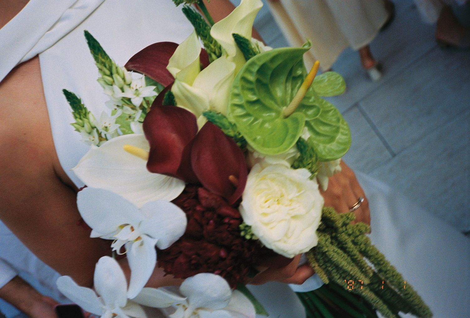 Elegant wedding bouquet featuring white orchids, calla lilies, green anthurium, and ivory roses held by a bride.