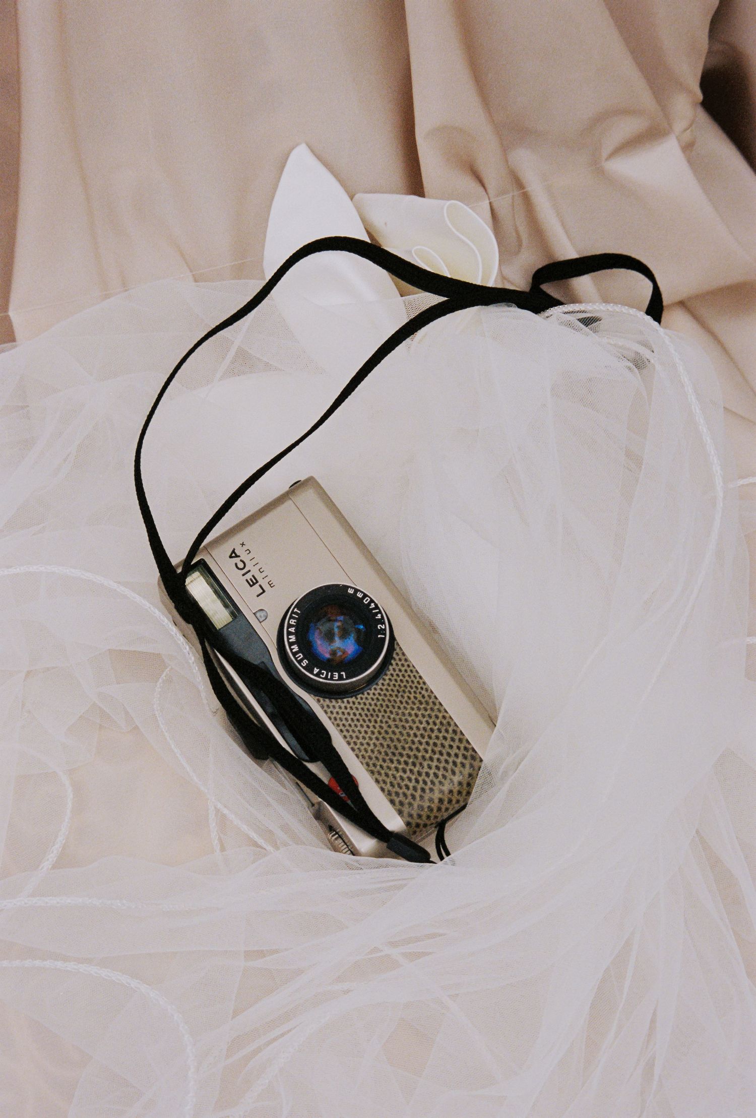 Vintage Leica camera with black strap resting on white tulle fabric near beige curtains.