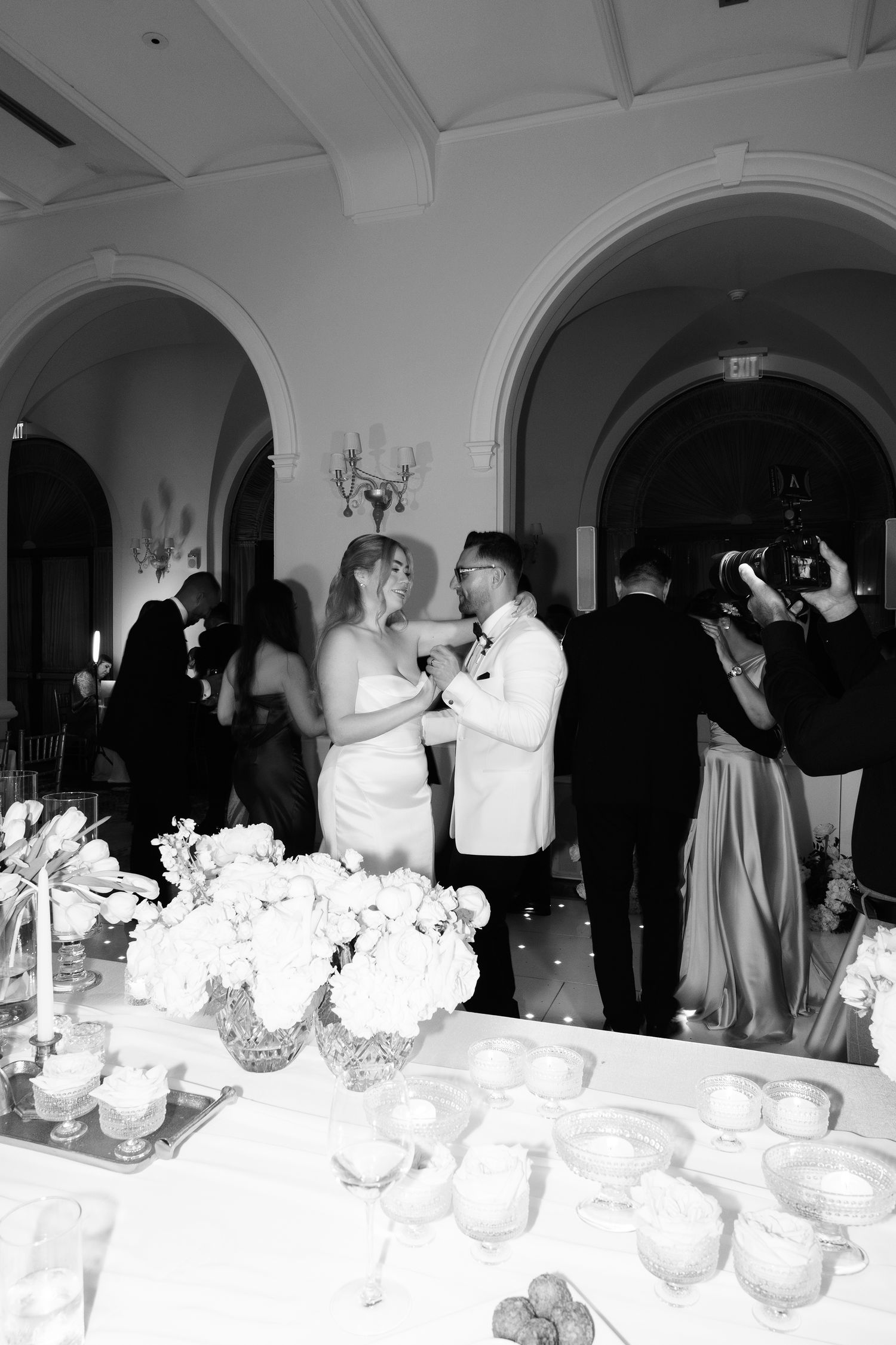 Reception tables decorated with white floral centerpieces and place settings in an elegant arched venue.