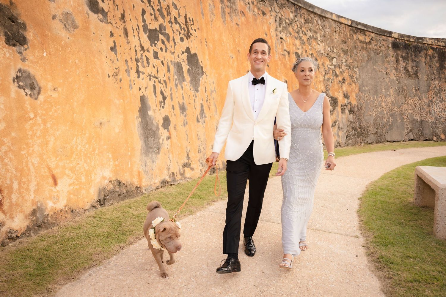 Wedding party walks along rustic orange stone wall pathway during photo session.