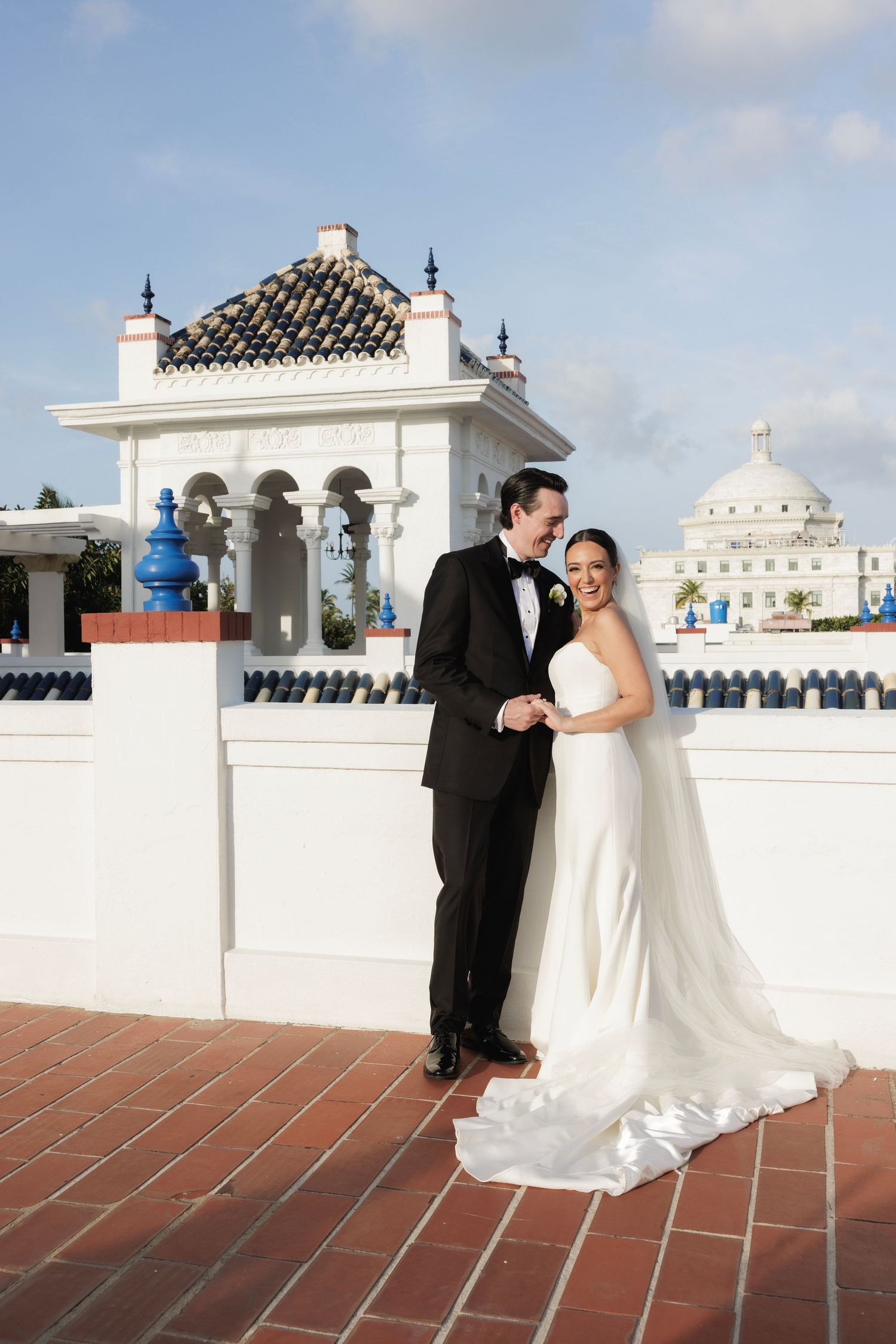 Wedding couple posing on a rooftop terrace with white Spanish colonial architecture and blue sky backdrop.