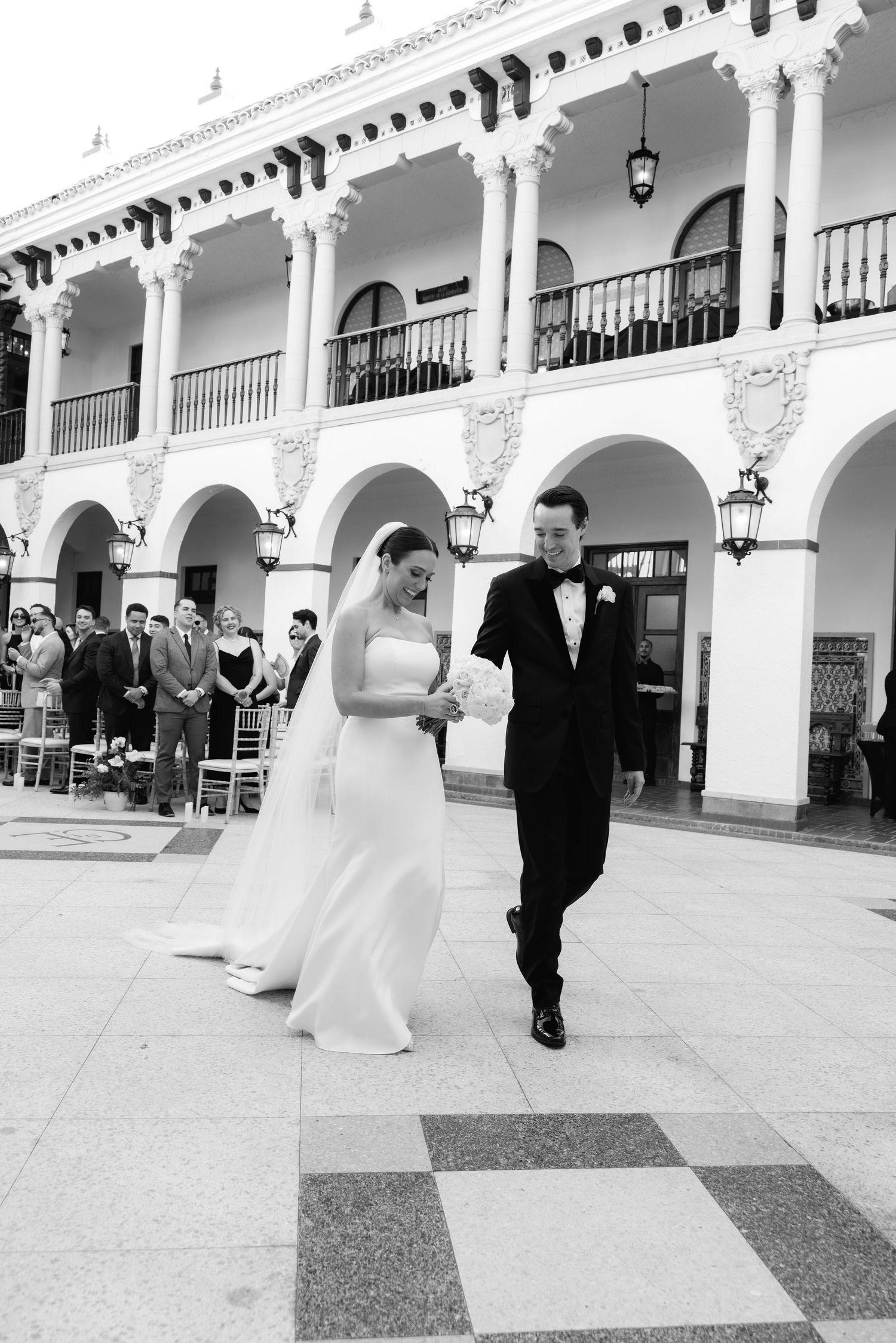 Black and white photo sequence of a couple walking through an ornate columned arcade.