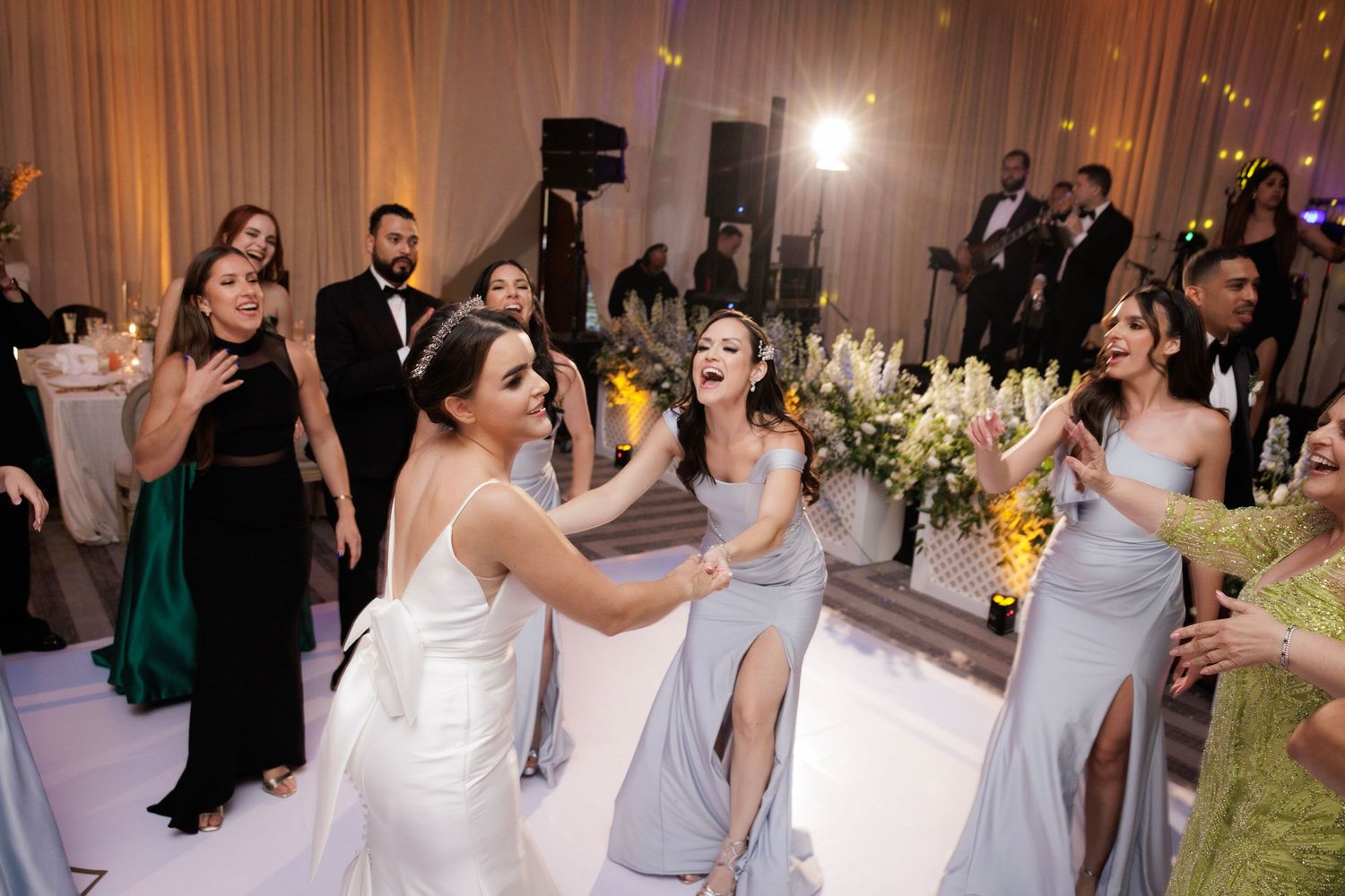 Wedding party guests dance joyfully on a reception dance floor while wearing formal evening attire.