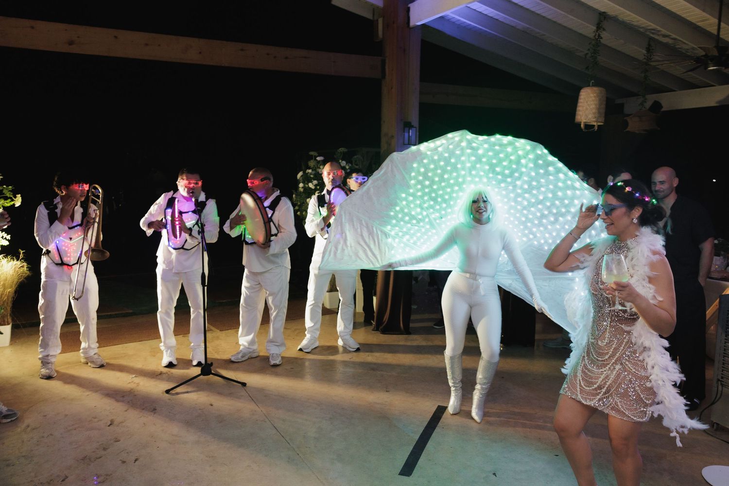 Dancers move across a dimly lit dance floor with blue and green lighting effects during a social event.