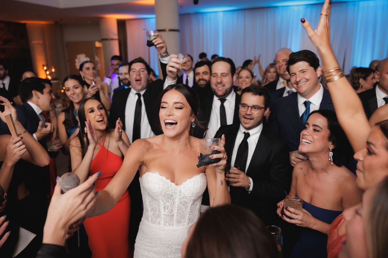 Joyful wedding reception crowd dancing together under colorful party lights.
