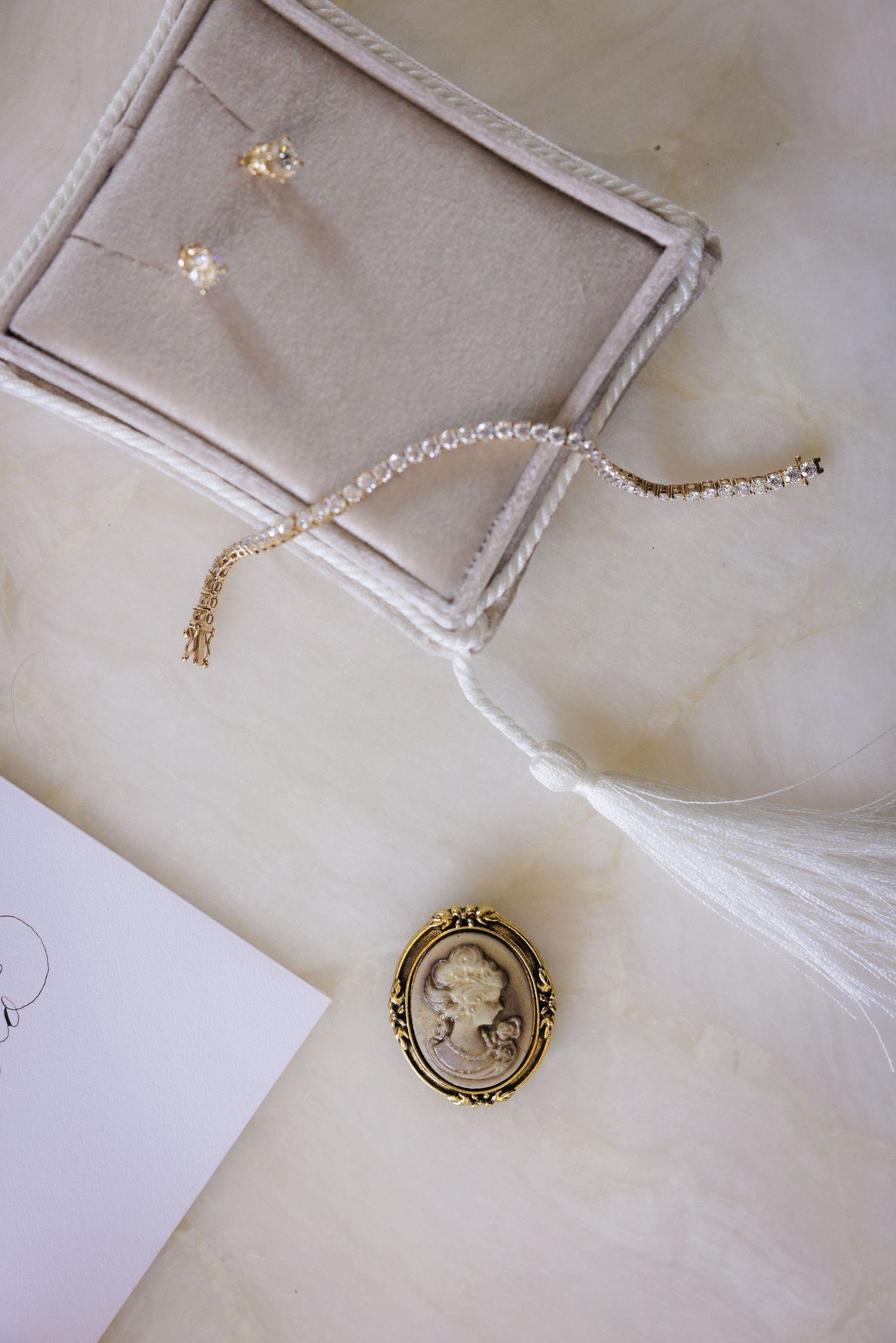 Wedding accessories including delicate jewelry, a pearl bracelet, and vintage cameo brooch on white surface.