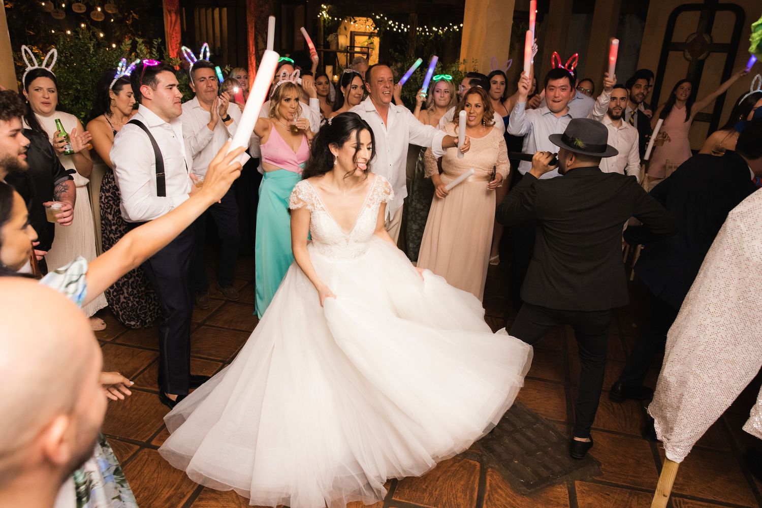 Wedding guests dance and celebrate on the reception dance floor beneath festive string lights and decorations.