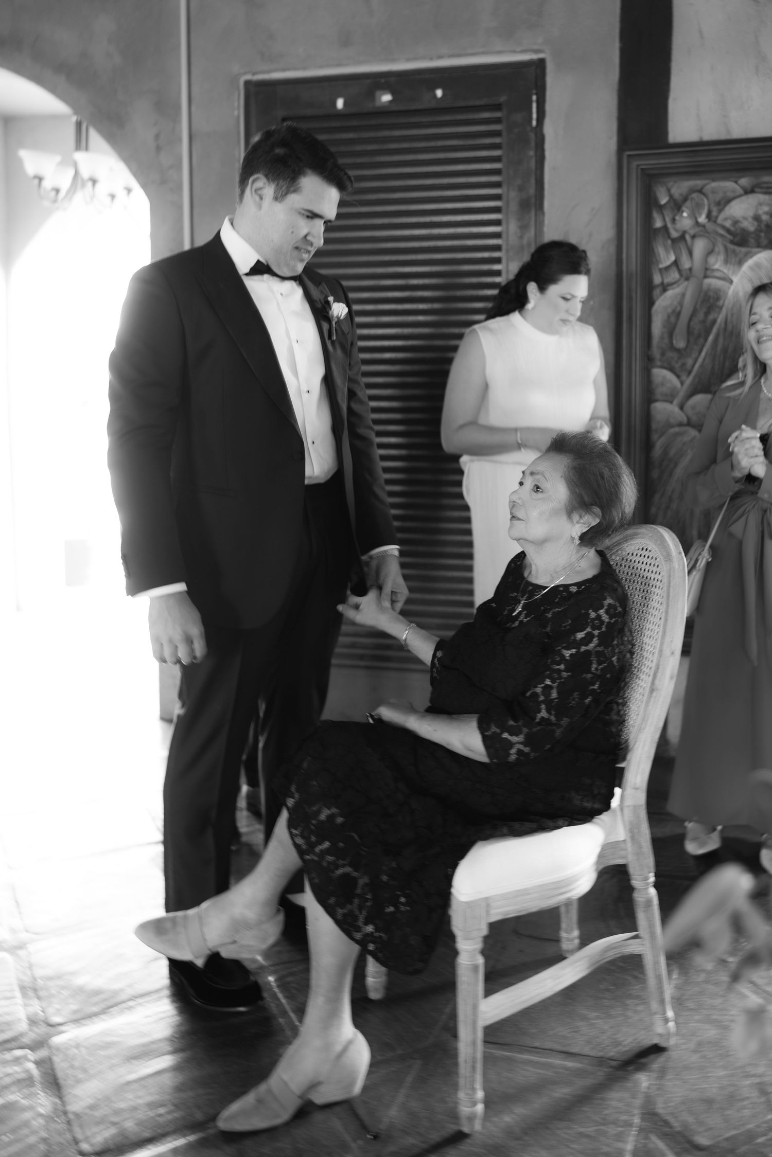 Wedding party helps with last minute shoe adjustments on a wooden floor.