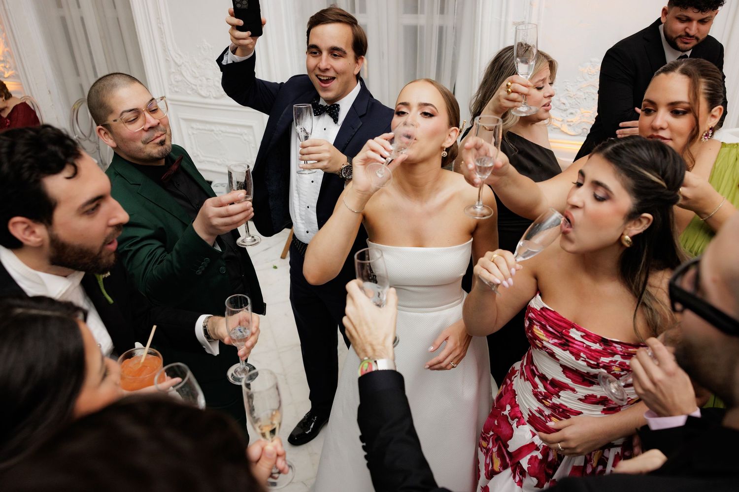 Wedding party guests raising champagne glasses and taking shots during a celebratory toast at a reception.