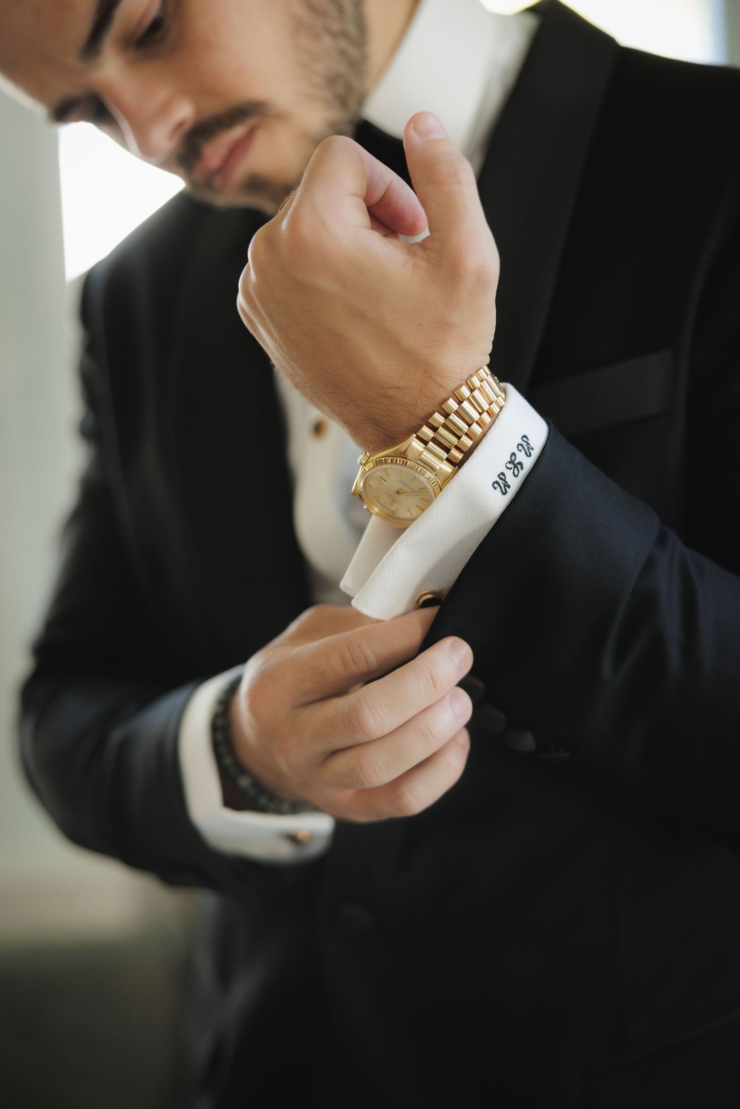 Close-up of hands adjusting gold watch and cufflink on formal black suit.