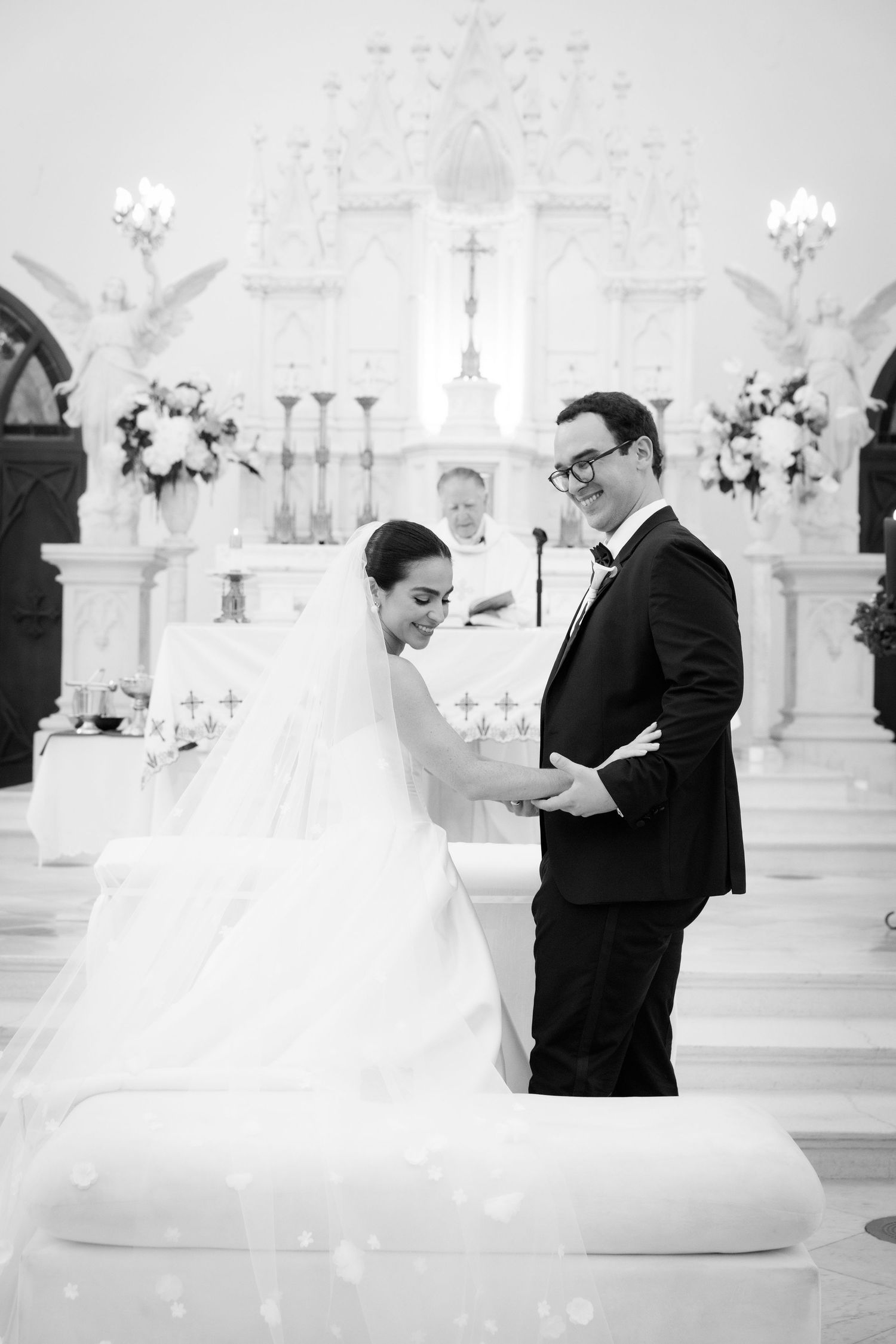 Black and white photo of wedding ceremony in traditional white church interior.