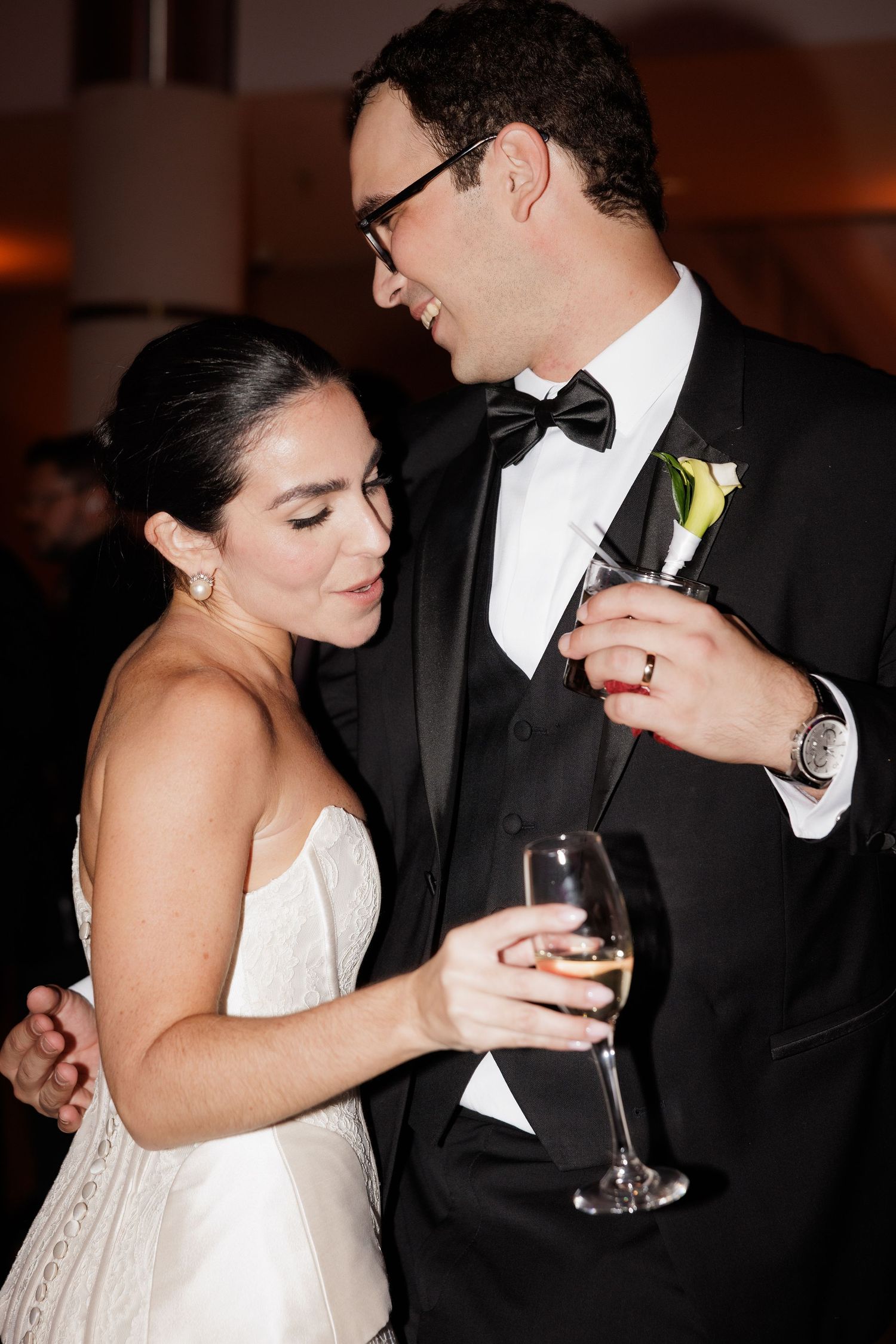 A bride and groom share an intimate moment at their wedding reception while holding champagne glasses.