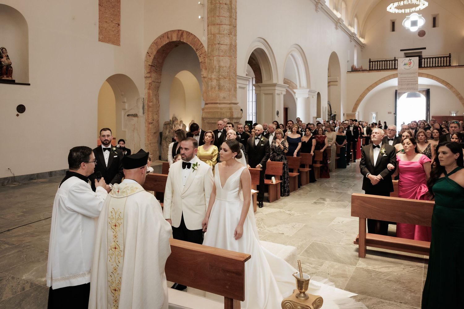 Traditional wedding ceremony taking place inside a historic church with arched columns and gathered guests.