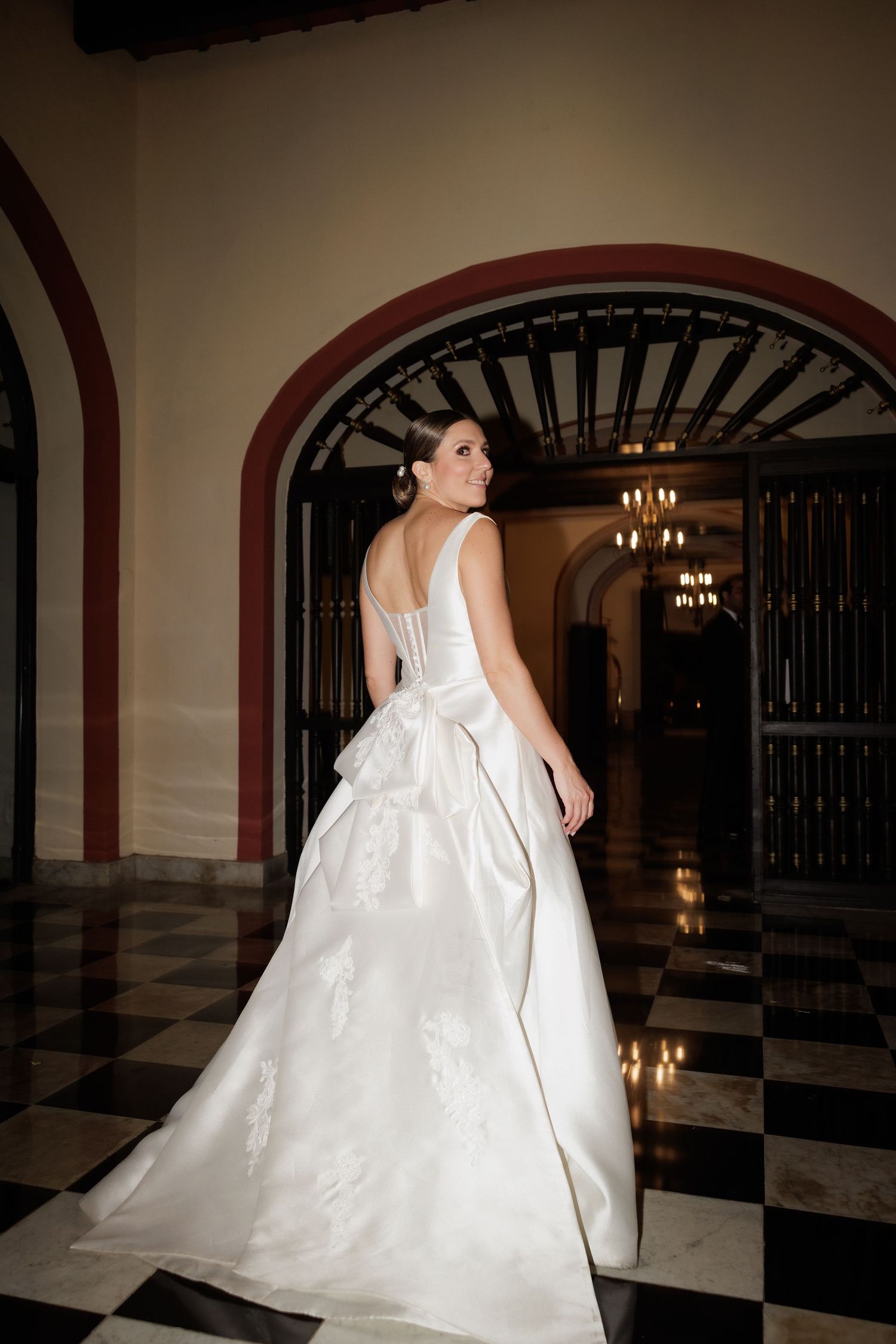 Elegant white wedding gown with dramatic train photographed in grand hallway with checkered floor and arched doorway.