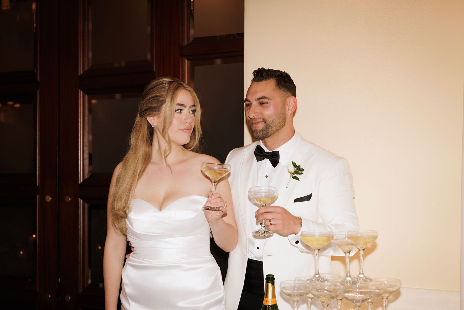 Bride and groom perform a traditional champagne tower pour at their wedding reception.