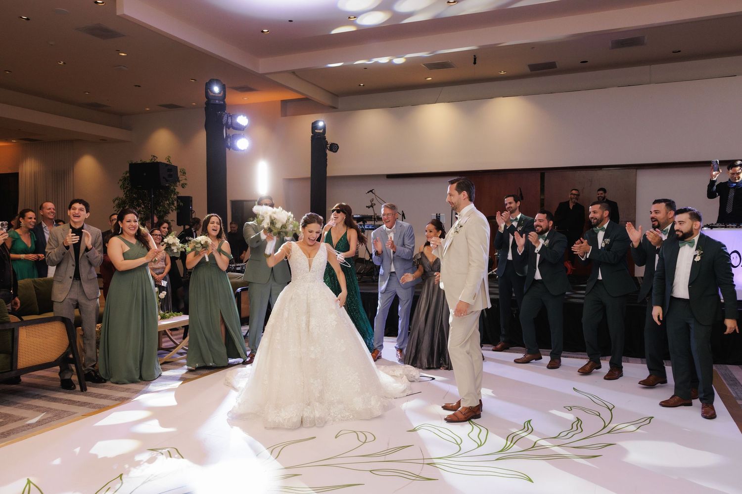 Elegantly dressed wedding guests form a circle on a dance floor around a couple in formal attire during a celebration.