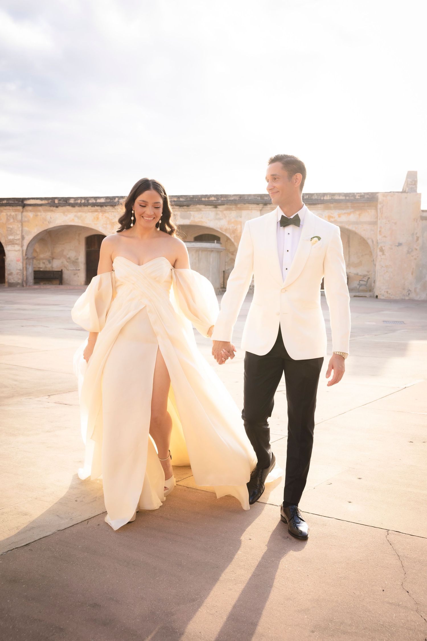Sunlit wedding photos featuring flowing dress and formal attire against stone architecture.